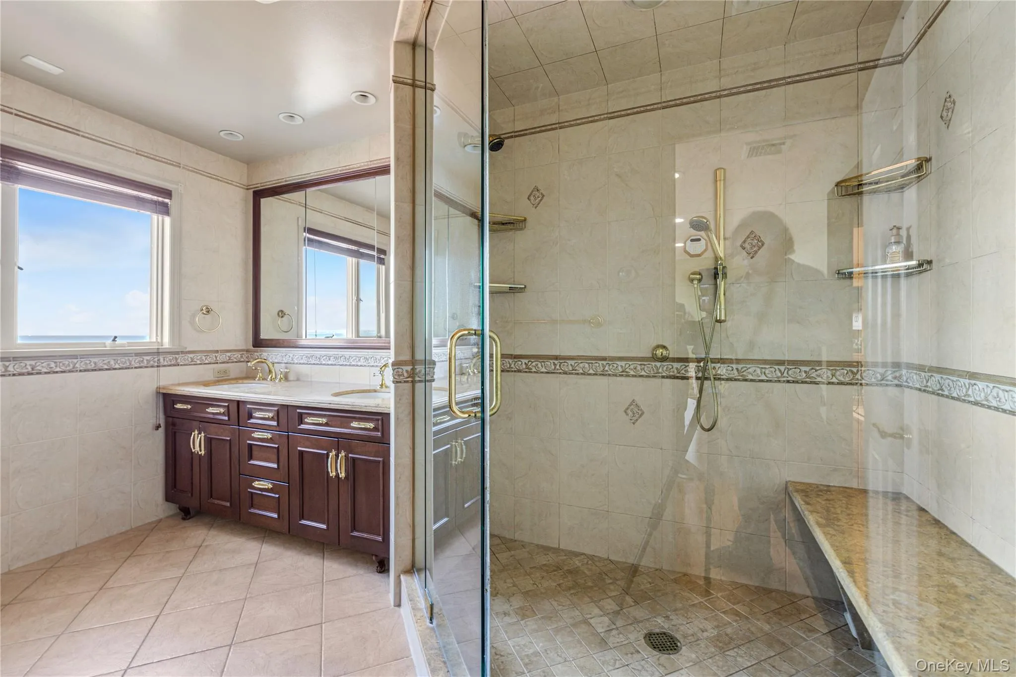 Bathroom featuring tile walls, double vanity, light tile patterned floors, and a stall shower Bathroom featuring tile walls, double vanity, light tile patterned floors, and a stall shower