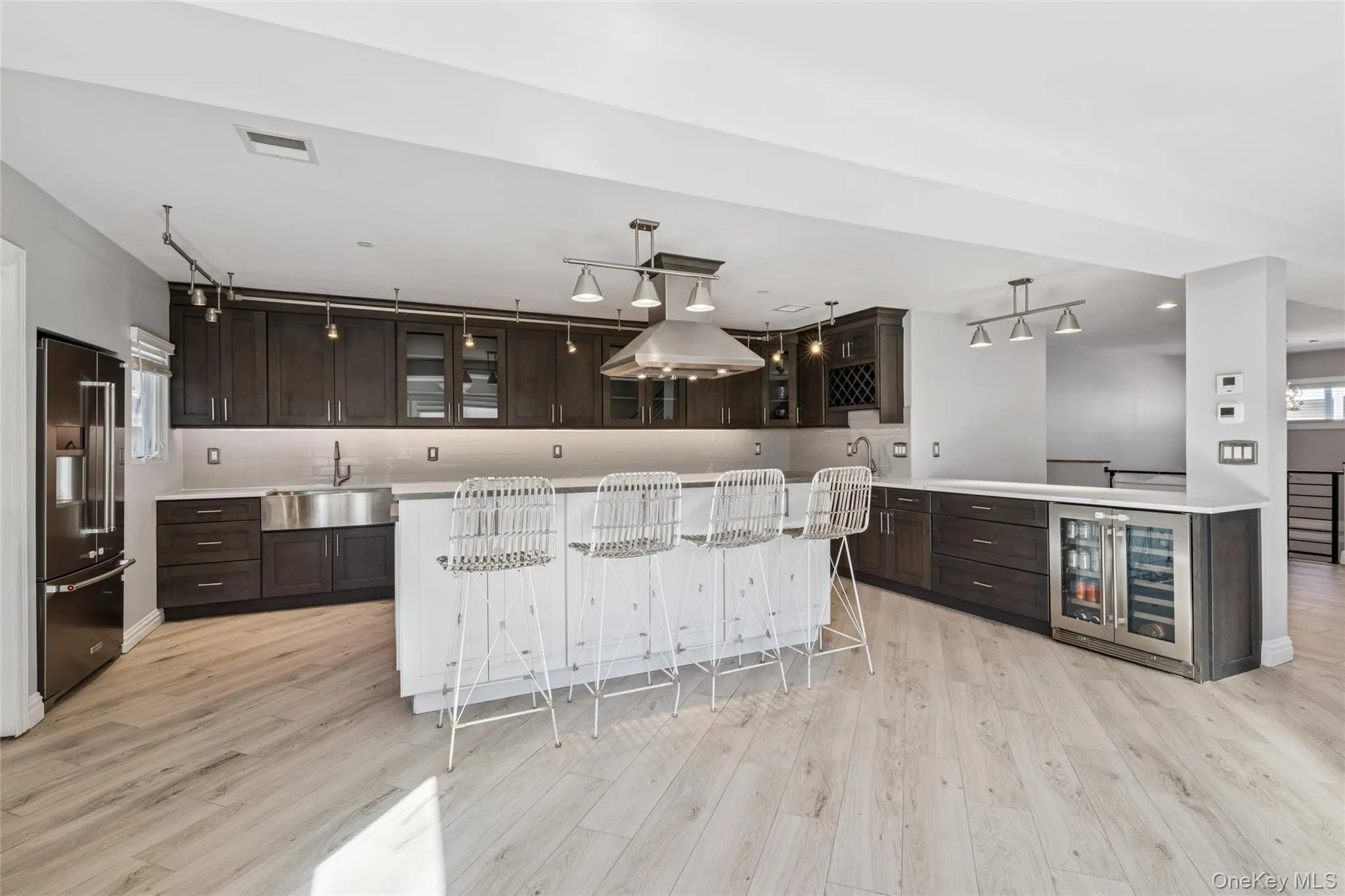 Indoor wet bar with dark brown cabinets, glass insert cabinets, light wood-type flooring, and recessed lighting Indoor wet bar with dark brown cabinets, glass insert cabinets, light wood-type flooring, and recessed lighting