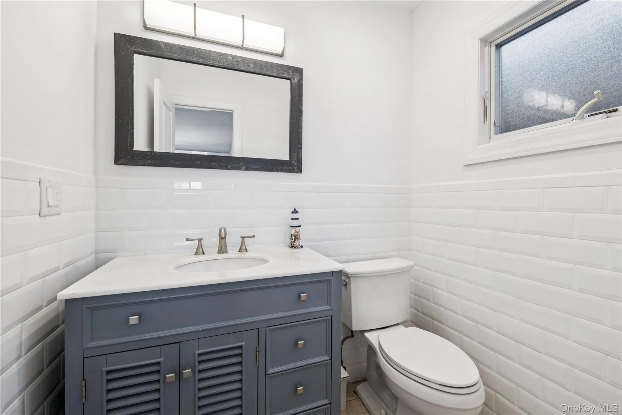 Half bathroom featuring tile walls, a wainscoted wall, and vanity Half bathroom featuring tile walls, a wainscoted wall, and vanity