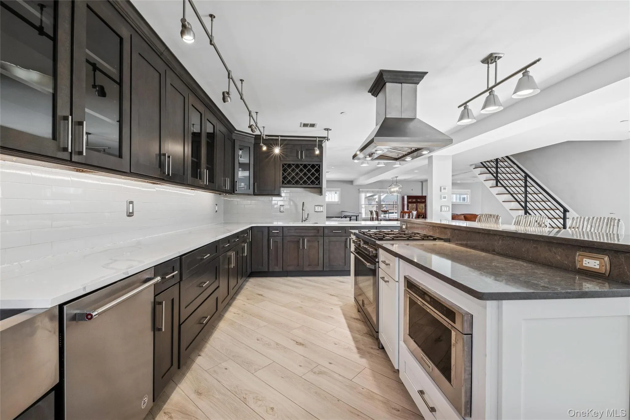 Kitchen with dark stone countertops, glass insert cabinets, island range hood, stainless steel appliances, and backsplash Kitchen with dark stone countertops, glass insert cabinets, island range hood, stainless steel appliances, and backsplash