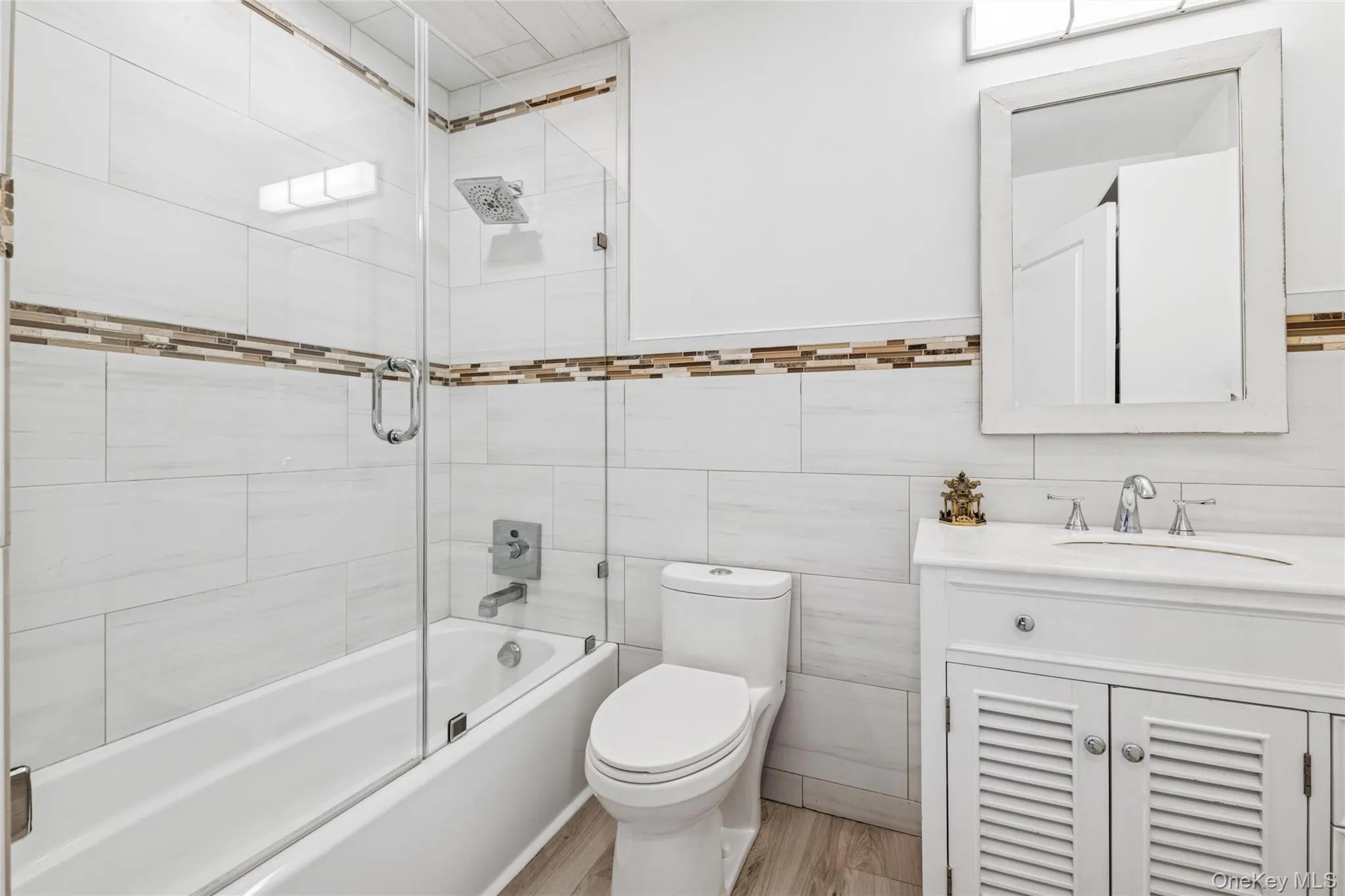 Bathroom with combined bath / shower with glass door, vanity, tile walls, and light wood-style floors Bathroom with combined bath / shower with glass door, vanity, tile walls, and light wood-style floors