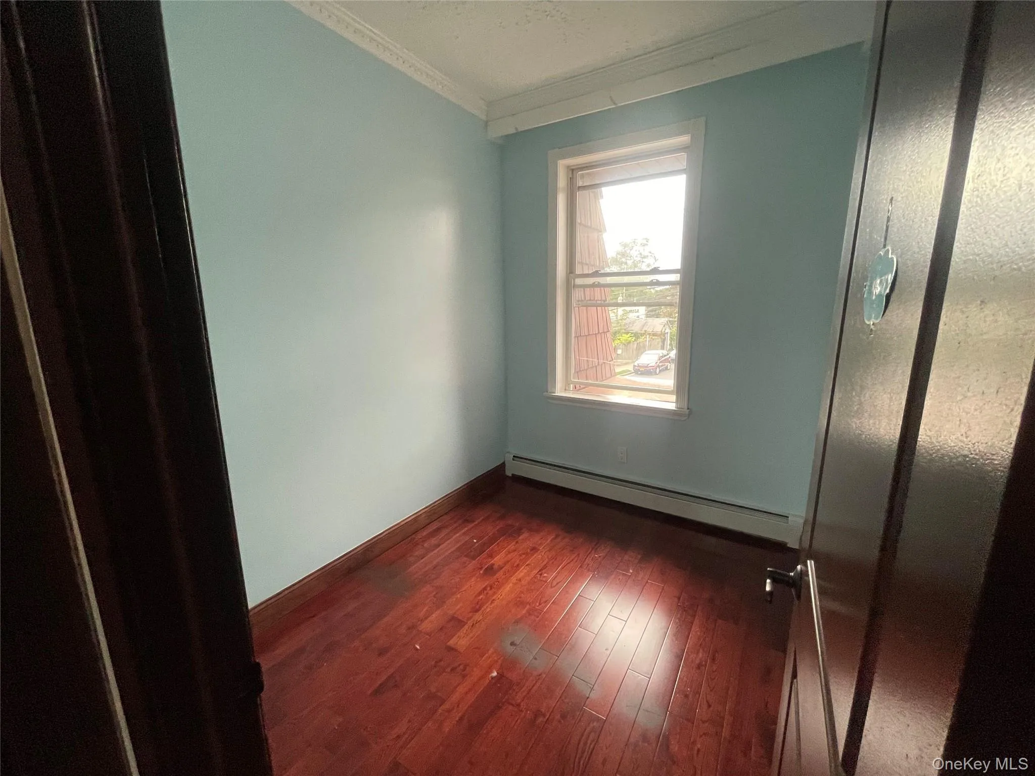 Unfurnished bedroom with dark wood-type flooring, baseboard heating, and ornamental molding Unfurnished bedroom with dark wood-type flooring, baseboard heating, and ornamental molding
