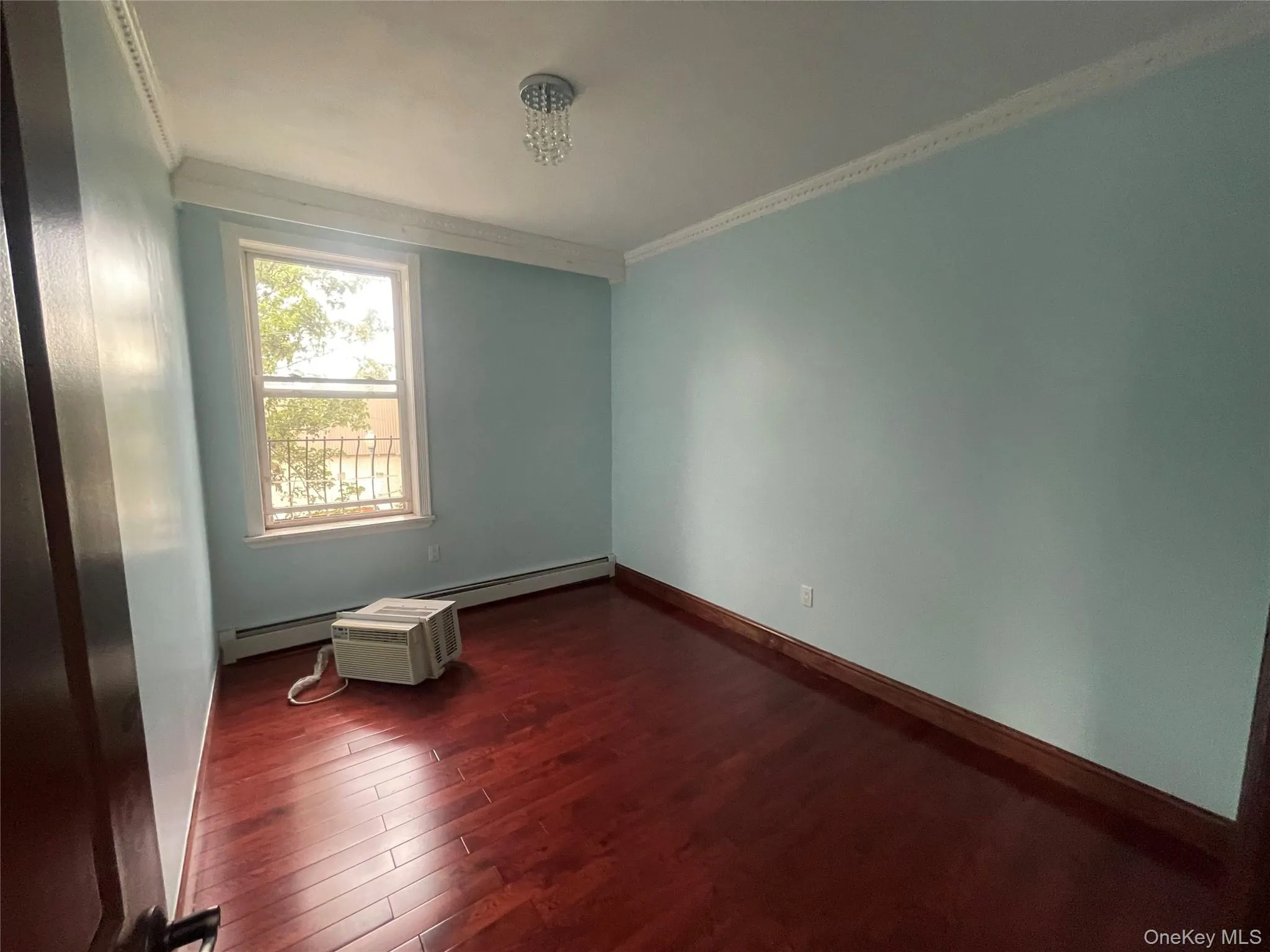 Unfurnished room with dark wood-style floors, crown molding, and a baseboard heating unit Unfurnished room with dark wood-style floors, crown molding, and a baseboard heating unit