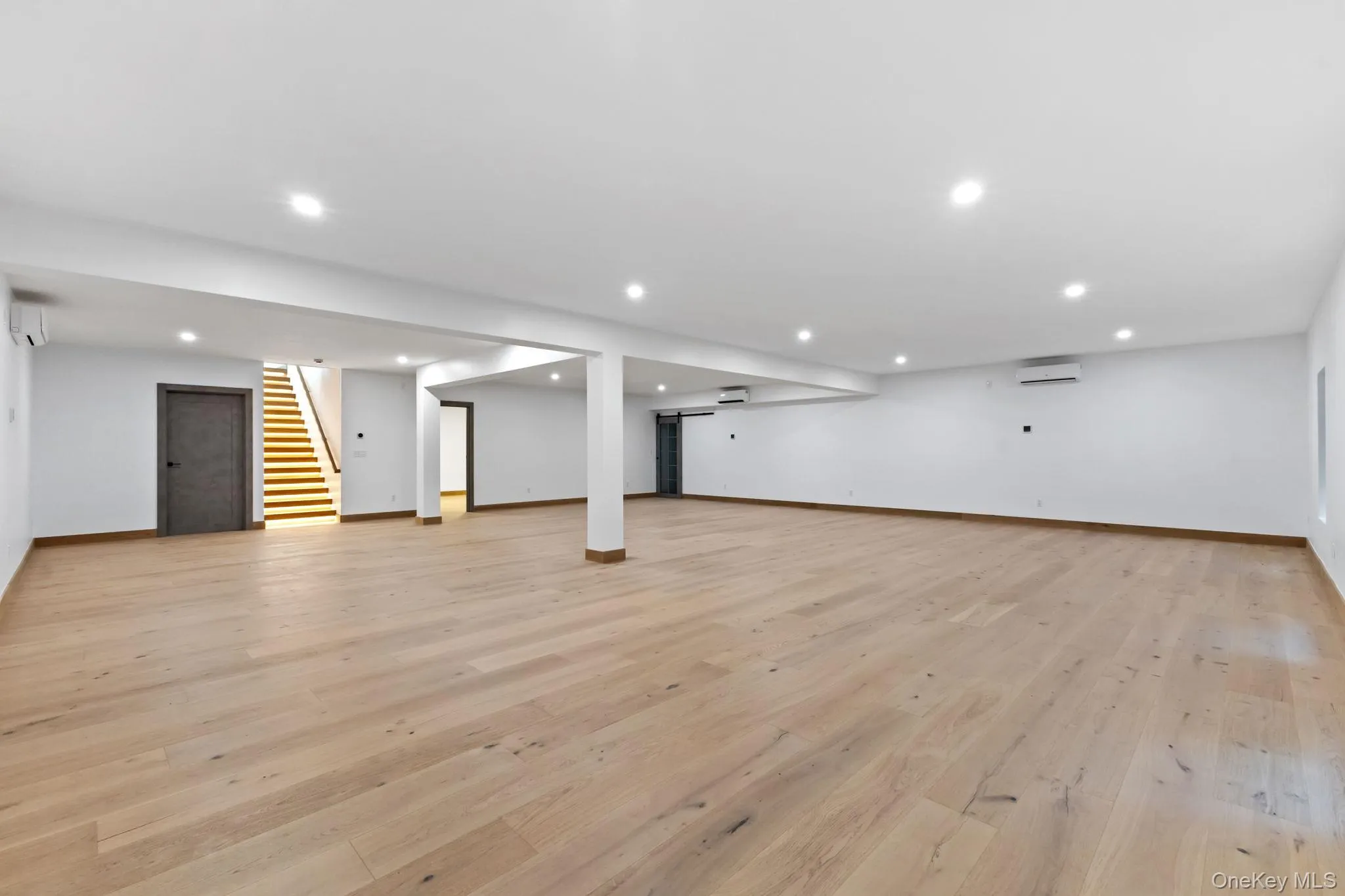 Finished below grade area featuring light wood-style floors, stairway, recessed lighting, and a wall mounted air conditioner Finished below grade area featuring light wood-style floors, stairway, recessed lighting, and a wall mounted air conditioner