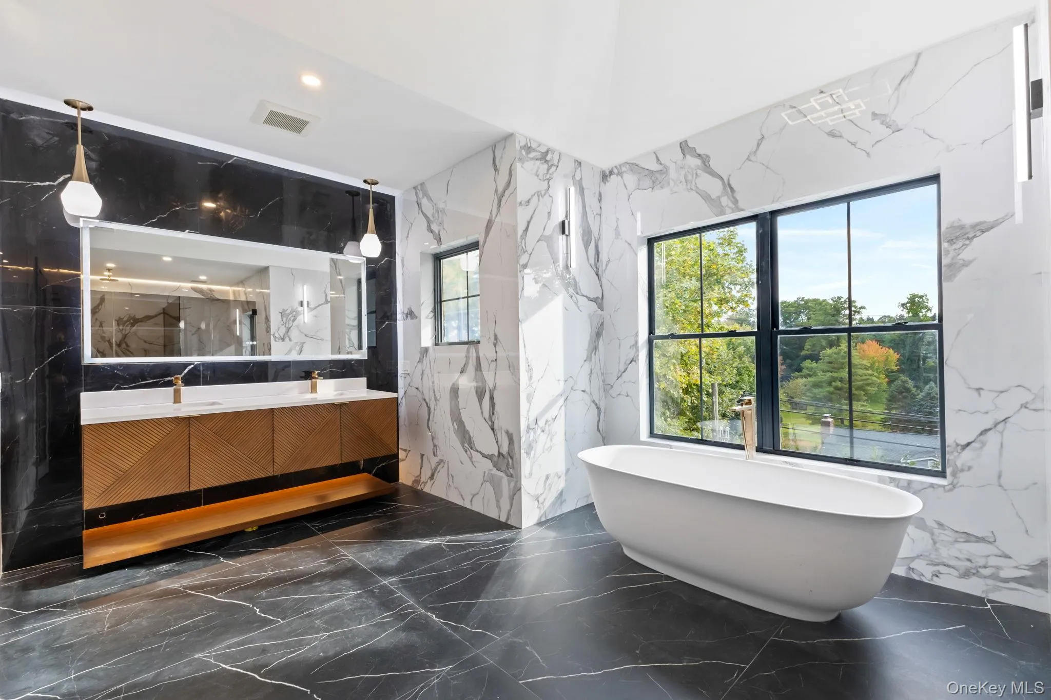 Bathroom featuring stone wall, dark marble finish flooring, double vanity, a freestanding tub, and recessed lighting Bathroom featuring stone wall, dark marble finish flooring, double vanity, a freestanding tub, and recessed lighting