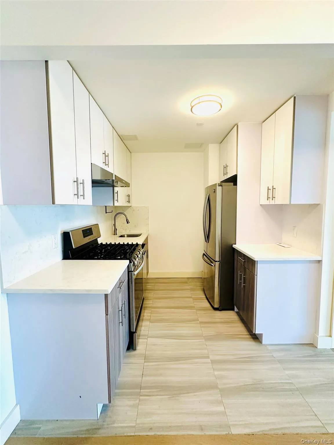 Kitchen featuring stainless steel appliances, white cabinets, light tile patterned floors, light stone counters, and under cabinet range hood Kitchen featuring stainless steel appliances, white cabinets, light tile patterned floors, light stone counters, and under cabinet range hood