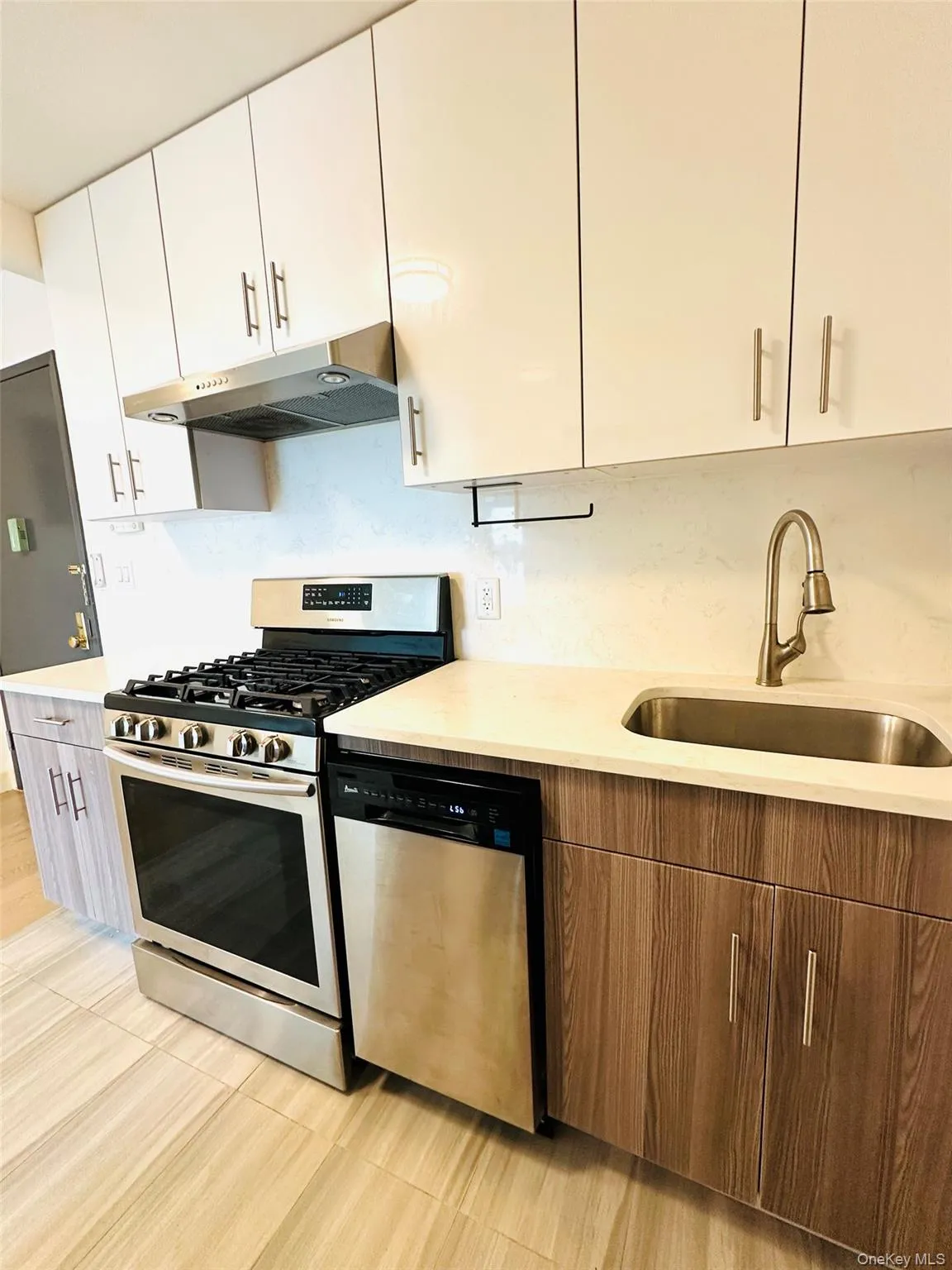 Kitchen with stainless steel appliances, white cabinetry, under cabinet range hood, modern cabinets, and light stone counters Kitchen with stainless steel appliances, white cabinetry, under cabinet range hood, modern cabinets, and light stone counters