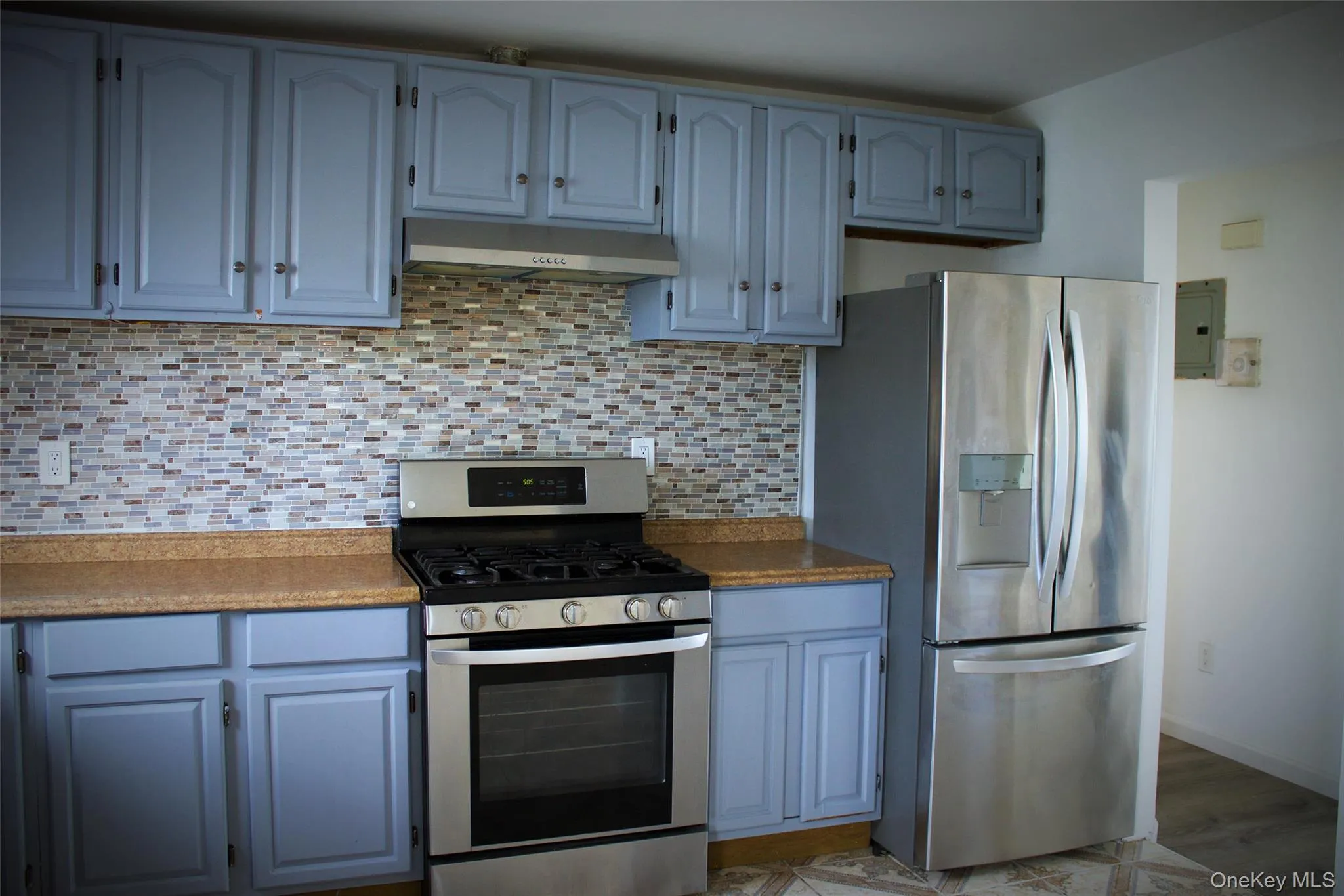 Kitchen featuring appliances with stainless steel finishes, blue cabinets, tasteful backsplash, under cabinet range hood, and electric panel Kitchen featuring appliances with stainless steel finishes, blue cabinets, tasteful backsplash, under cabinet range hood, and electric panel