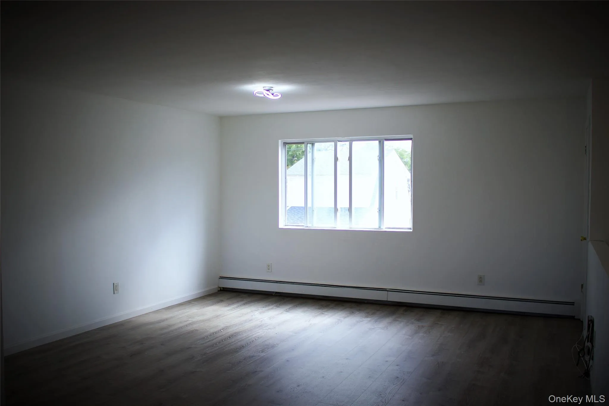 Unfurnished room with baseboard heating and dark wood finished floors Unfurnished room with baseboard heating and dark wood finished floors