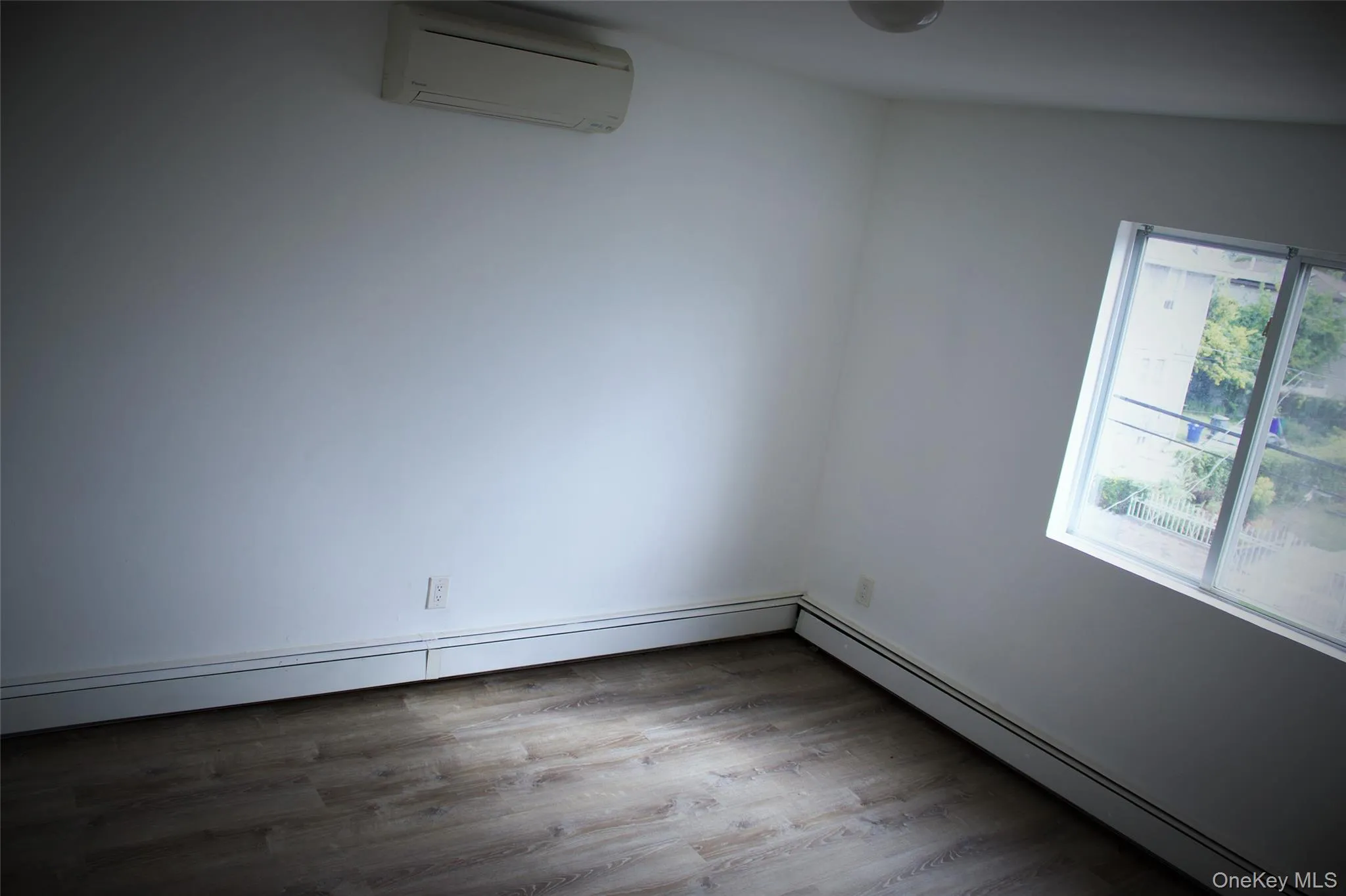 Empty room featuring baseboard heating, an AC wall unit, and light wood finished floors Empty room featuring baseboard heating, an AC wall unit, and light wood finished floors