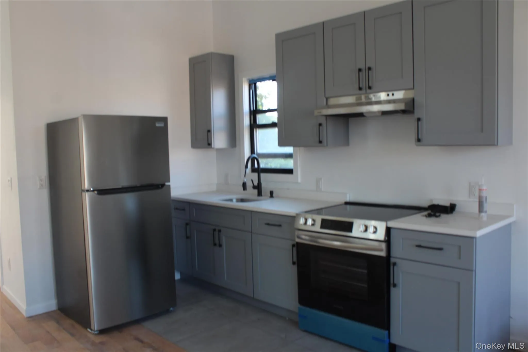 Kitchen with gray cabinets, appliances with stainless steel finishes, under cabinet range hood, and light wood-type flooring Kitchen with gray cabinets, appliances with stainless steel finishes, under cabinet range hood, and light wood-type flooring