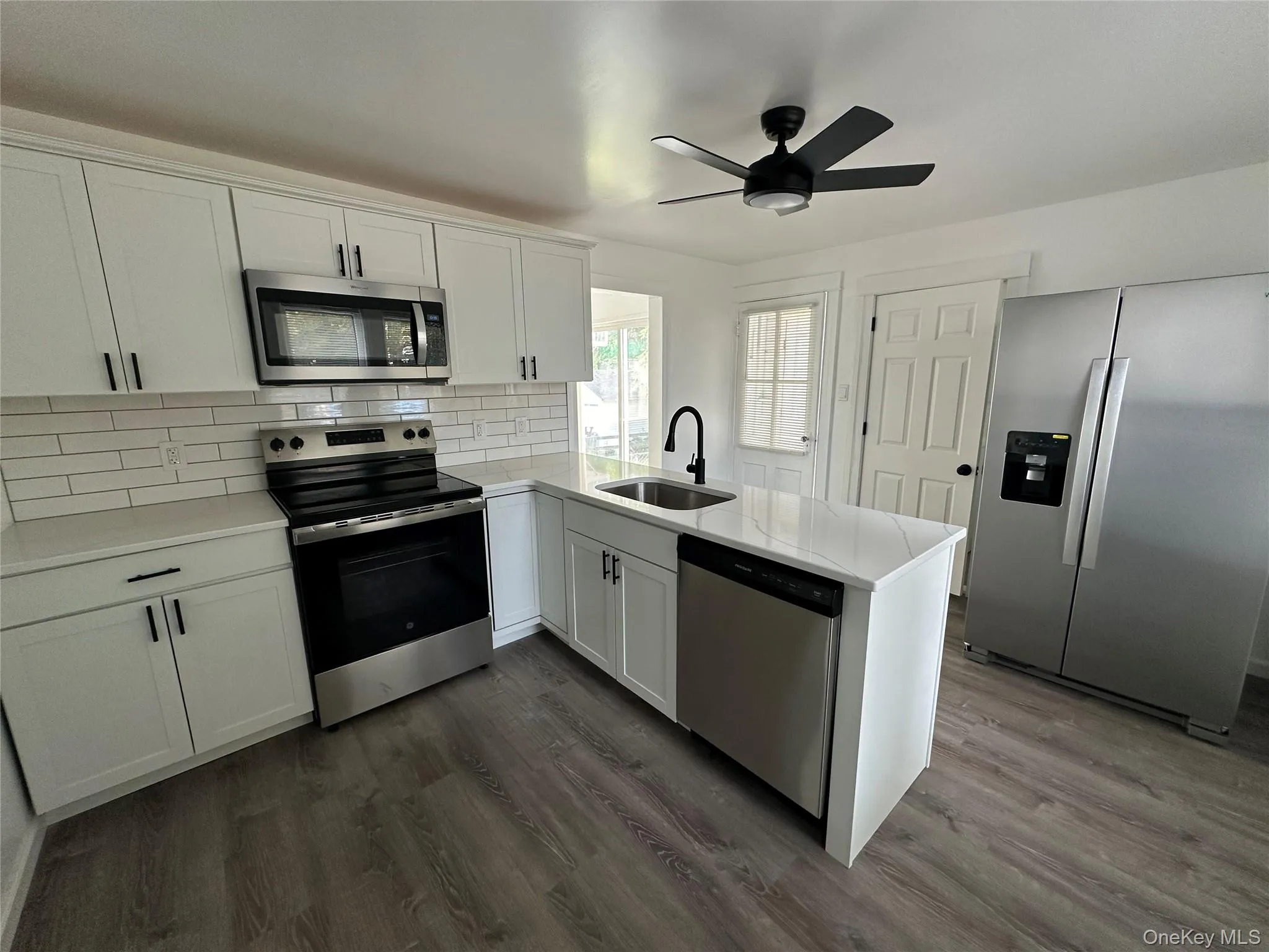 Kitchen featuring a peninsula, stainless steel appliances, backsplash, white cabinets, and dark wood finished floors Kitchen featuring a peninsula, stainless steel appliances, backsplash, white cabinets, and dark wood finished floors