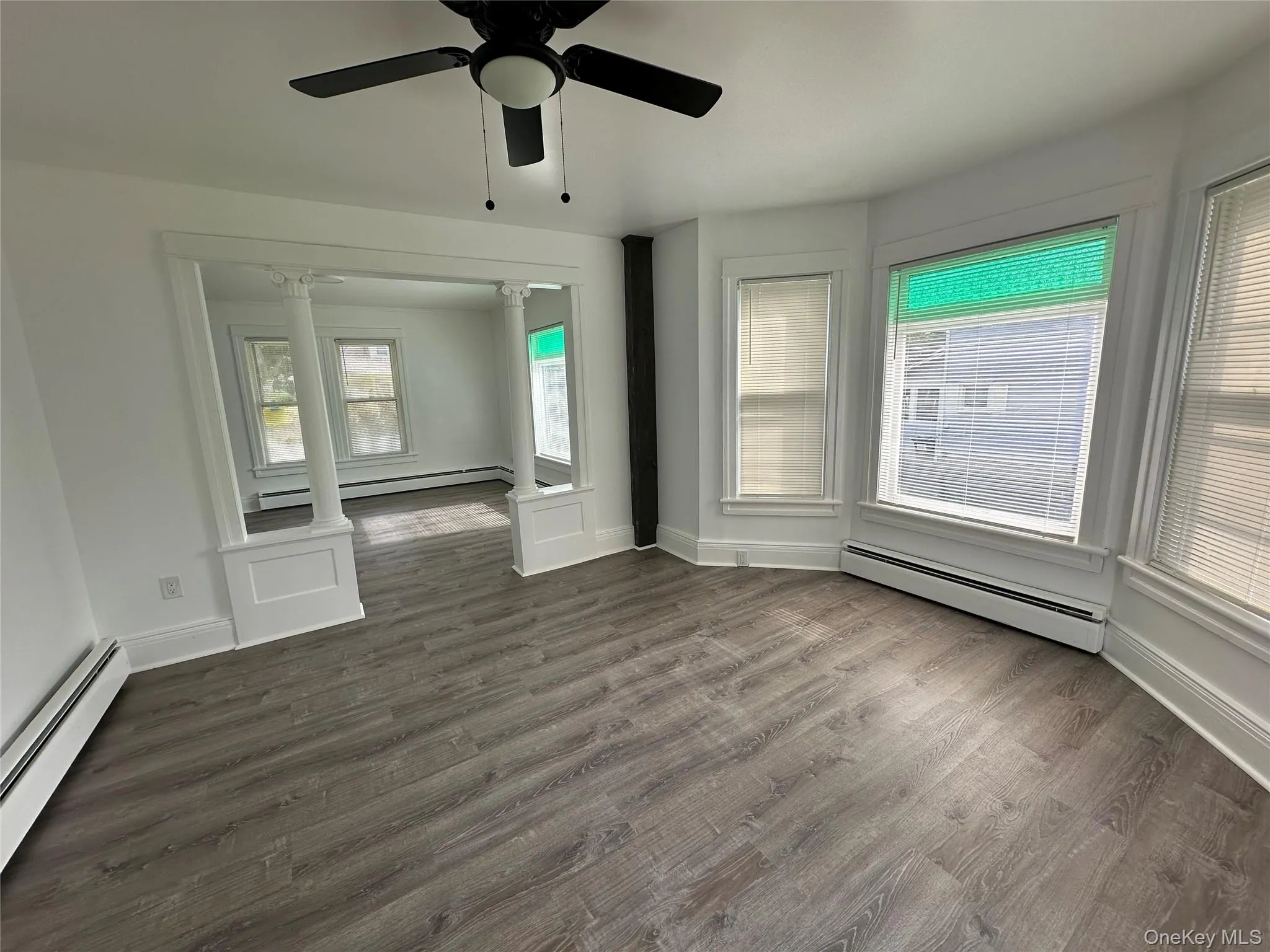 Unfurnished room featuring dark wood-style floors, a baseboard heating unit, ornate columns, and ceiling fan Unfurnished room featuring dark wood-style floors, a baseboard heating unit, ornate columns, and ceiling fan