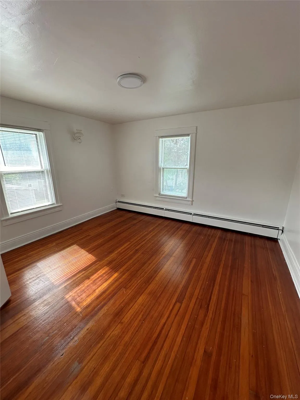 Empty room featuring hardwood / wood-style floors and a baseboard radiator Empty room featuring hardwood / wood-style floors and a baseboard radiator