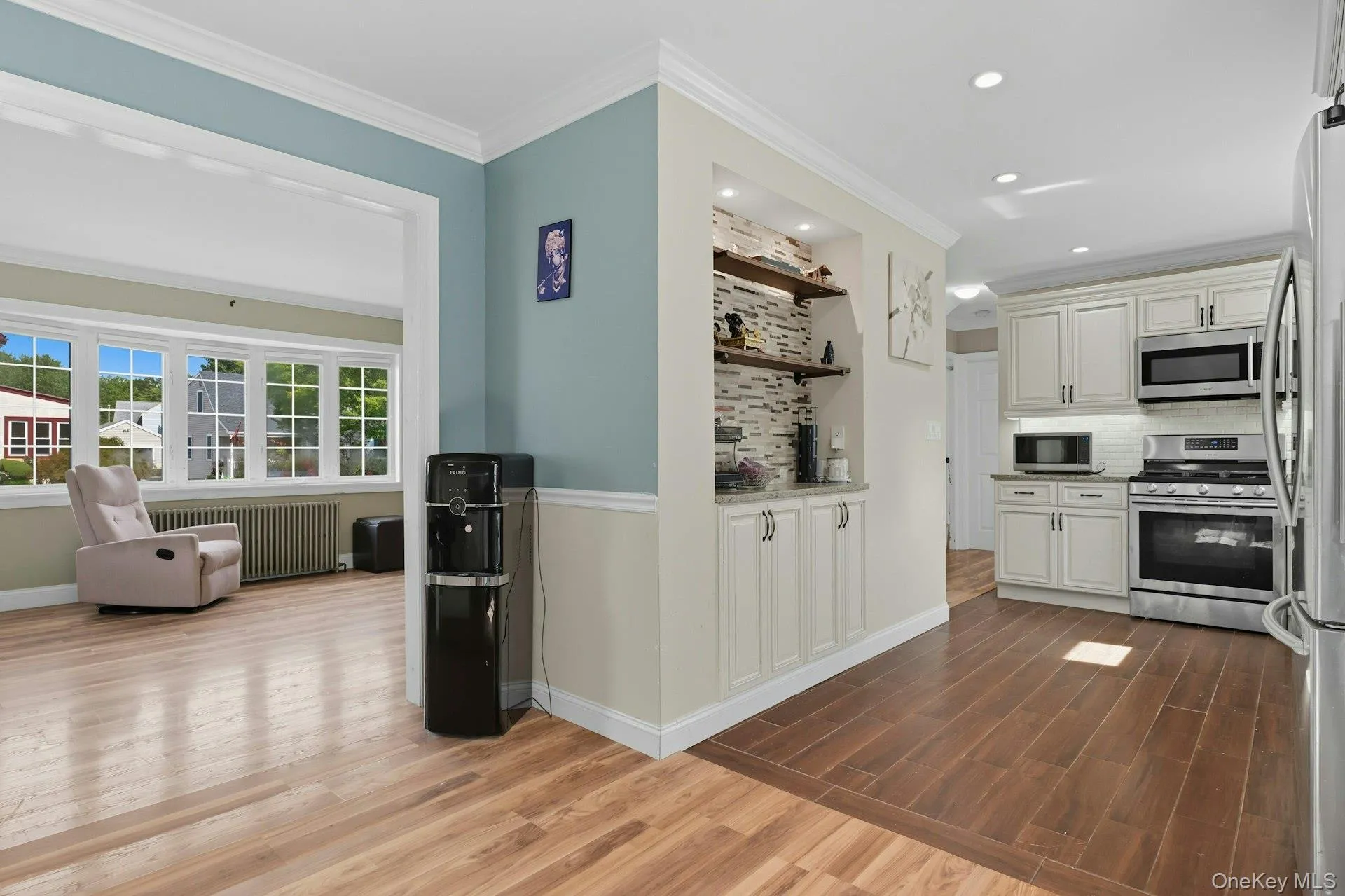 Kitchen featuring dark wood finished floors, backsplash, stainless steel appliances, radiator heating unit, and ornamental molding Kitchen featuring dark wood finished floors, backsplash, stainless steel appliances, radiator heating unit, and ornamental molding