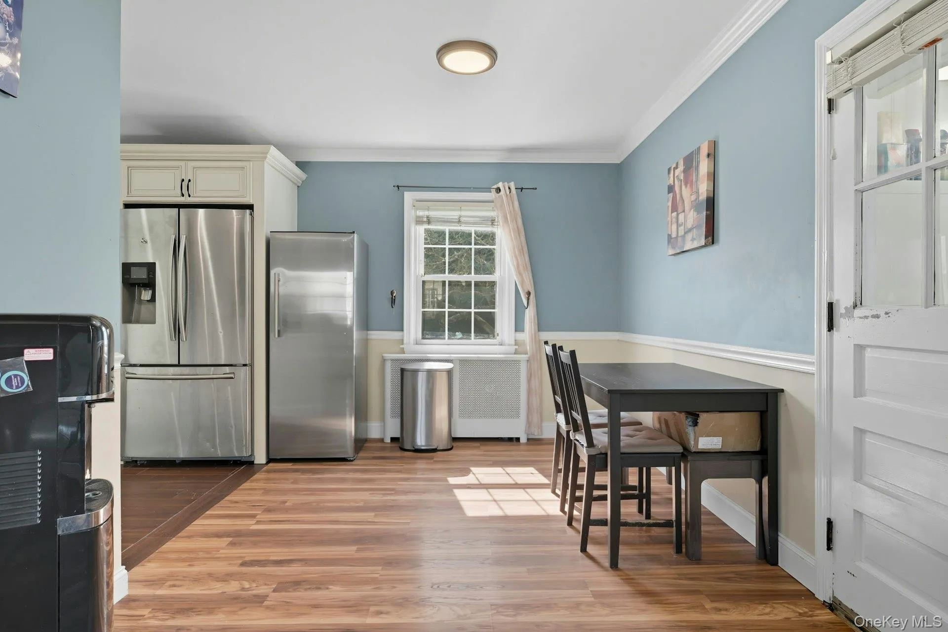 Kitchen with stainless steel fridge with ice dispenser, freestanding refrigerator, light wood-style flooring, ornamental molding, and radiator heating unit Kitchen with stainless steel fridge with ice dispenser, freestanding refrigerator, light wood-style flooring, ornamental molding, and radiator heating unit
