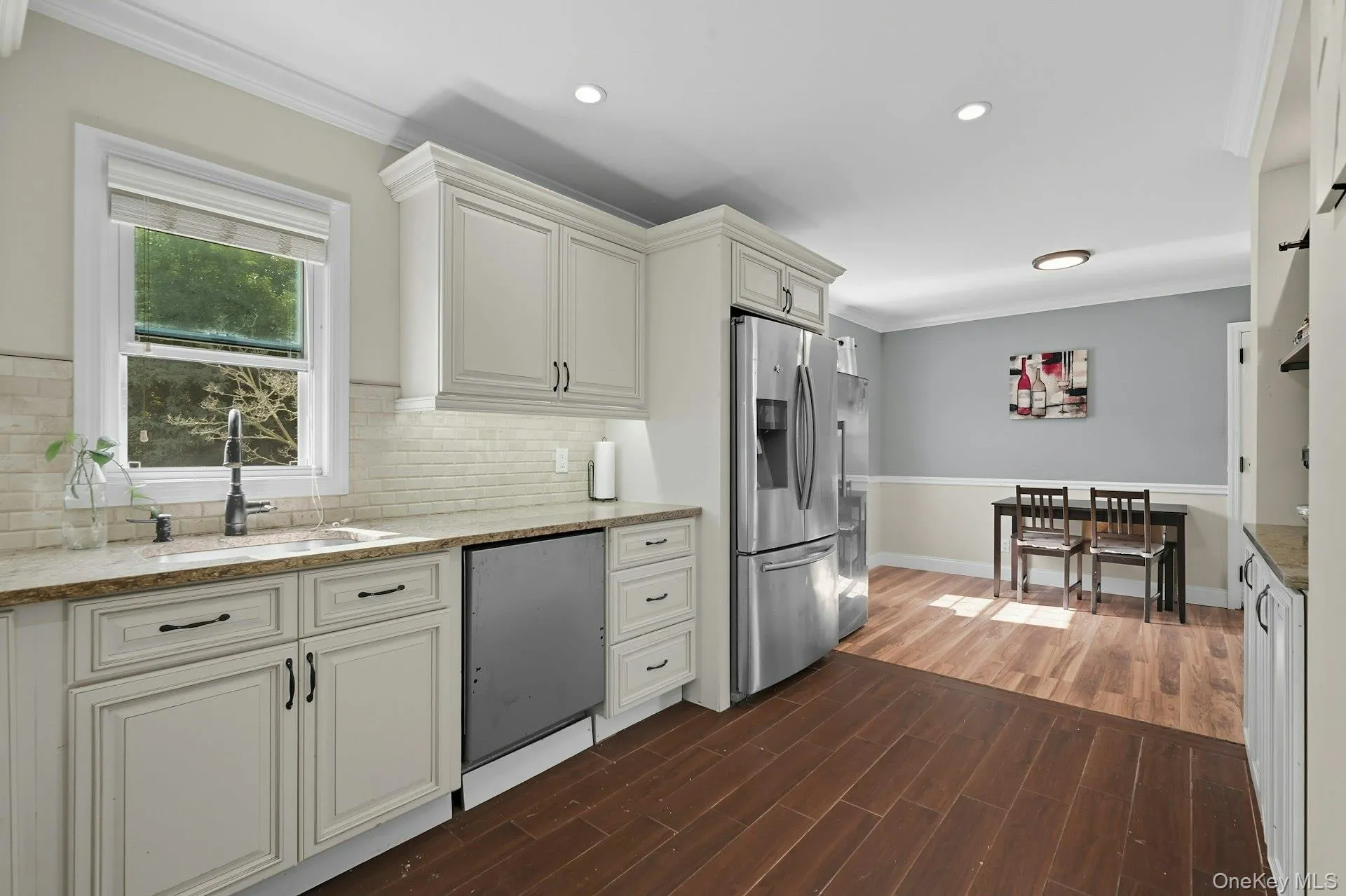 Kitchen featuring crown molding, dark wood-type flooring, stainless steel refrigerator with ice dispenser, light stone countertops Kitchen featuring crown molding, dark wood-type flooring, stainless steel refrigerator with ice dispenser, light stone countertops