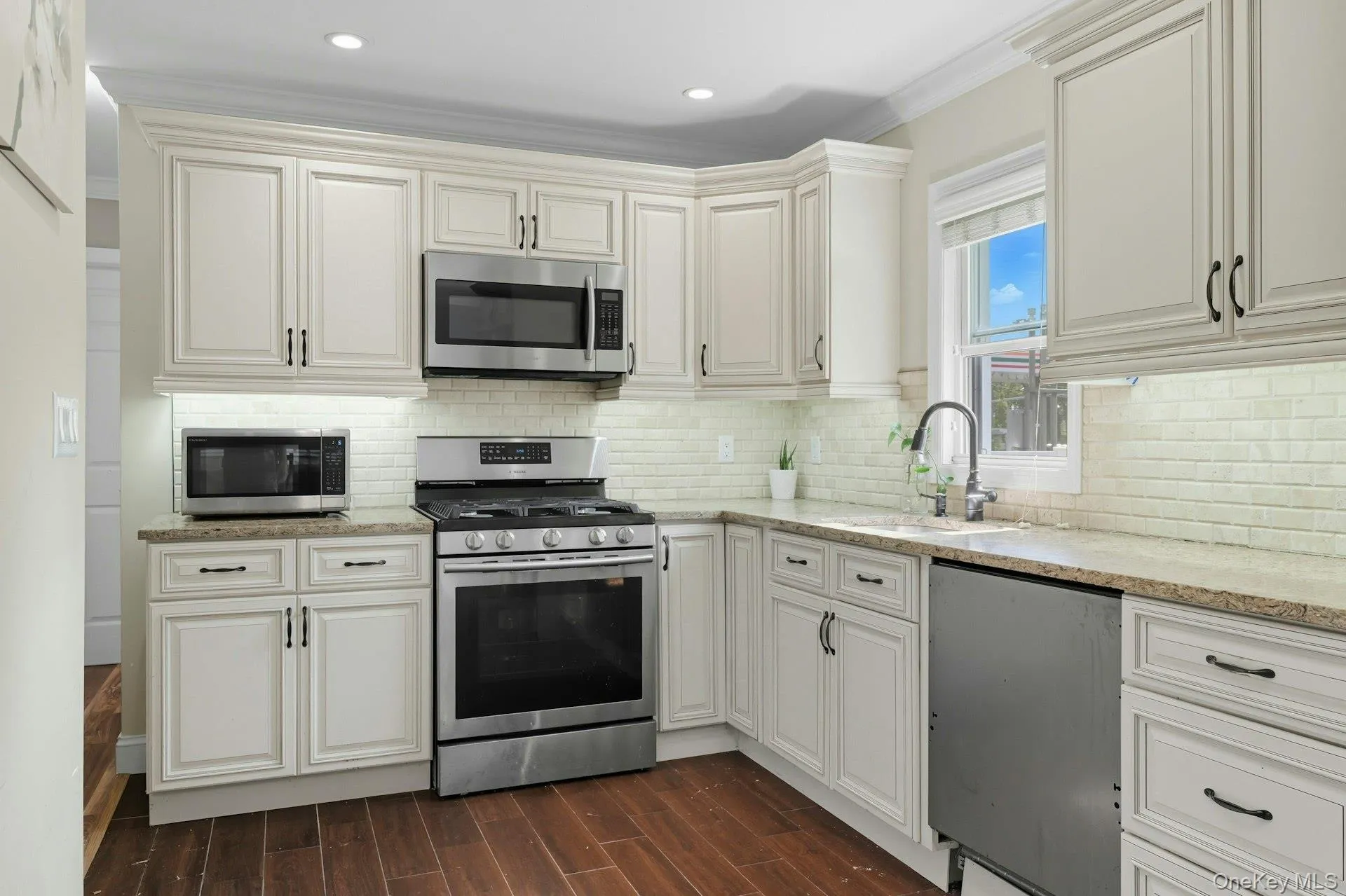 Kitchen with appliances with stainless steel finishes, wood tiled floors, light stone countertops, tasteful backsplash, and ornamental molding Kitchen with appliances with stainless steel finishes, wood tiled floors, light stone countertops, tasteful backsplash, and ornamental molding