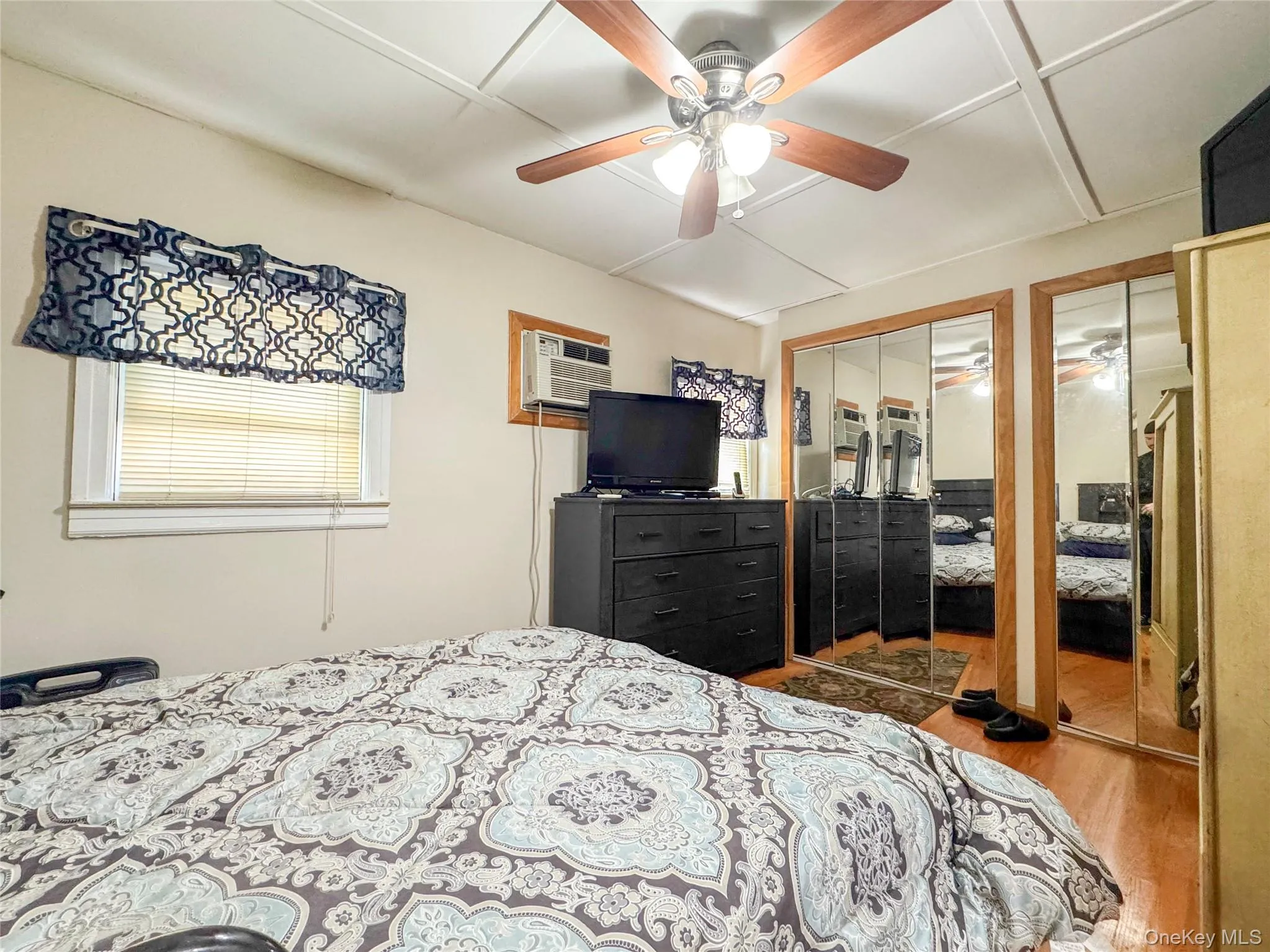 Bedroom featuring multiple closets, wood finished floors, a ceiling fan, and a wall unit AC Bedroom featuring multiple closets, wood finished floors, a ceiling fan, and a wall unit AC