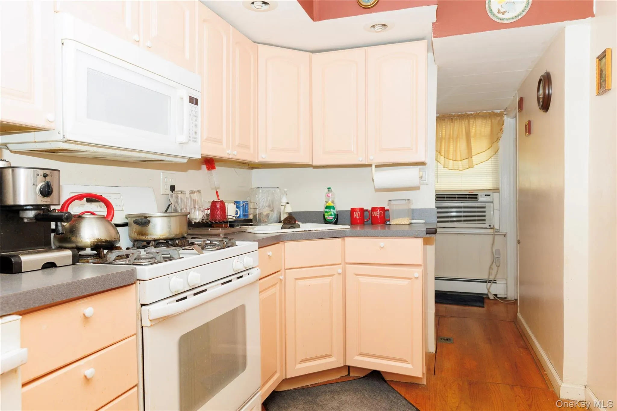 Kitchen with white appliances, dark wood finished floors, a baseboard heating unit, dark countertops, and cooling unit Kitchen with white appliances, dark wood finished floors, a baseboard heating unit, dark countertops, and cooling unit