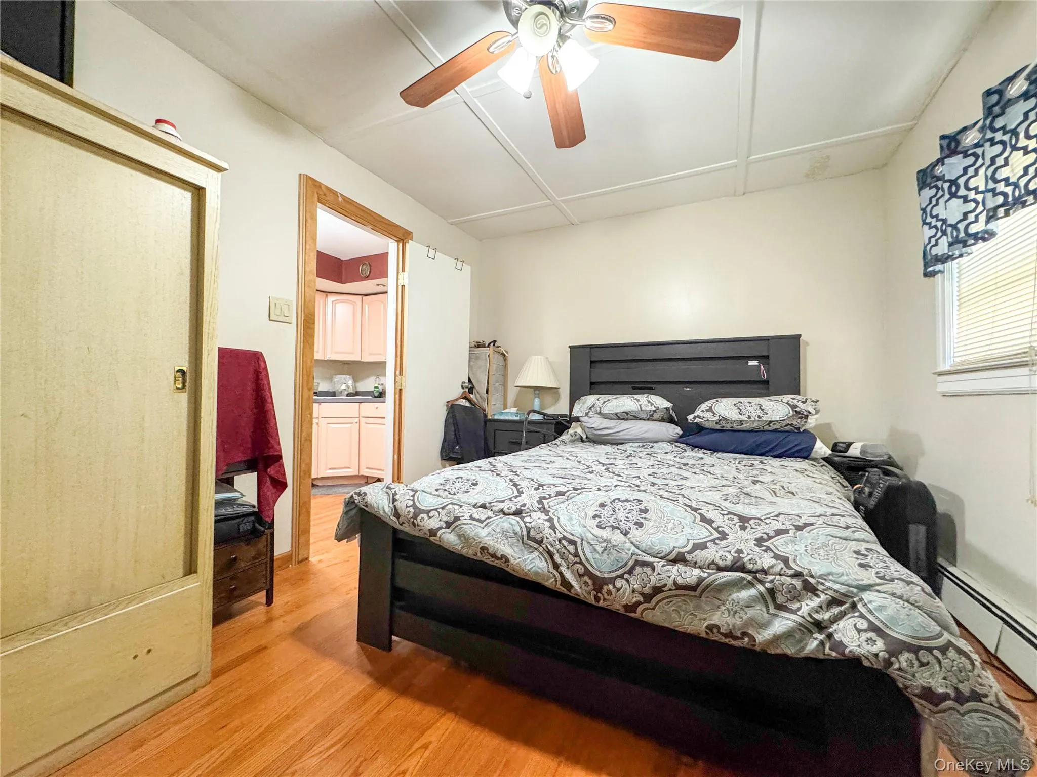 Bedroom featuring light wood-style flooring, a baseboard radiator, and a ceiling fan Bedroom featuring light wood-style flooring, a baseboard radiator, and a ceiling fan