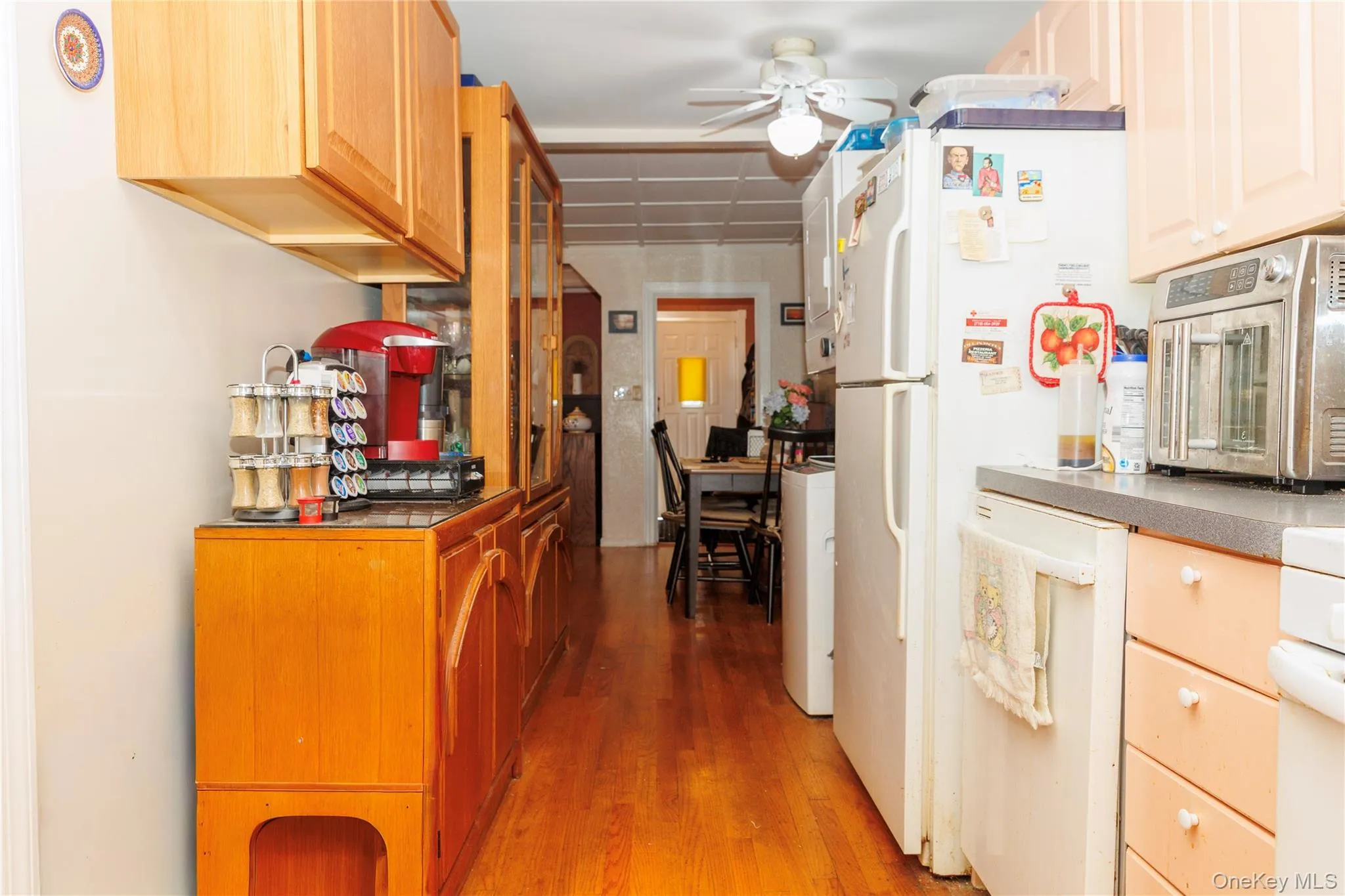 Kitchen with light wood-type flooring, dark countertops, a ceiling fan, white appliances, and glass insert cabinets Kitchen with light wood-type flooring, dark countertops, a ceiling fan, white appliances, and glass insert cabinets
