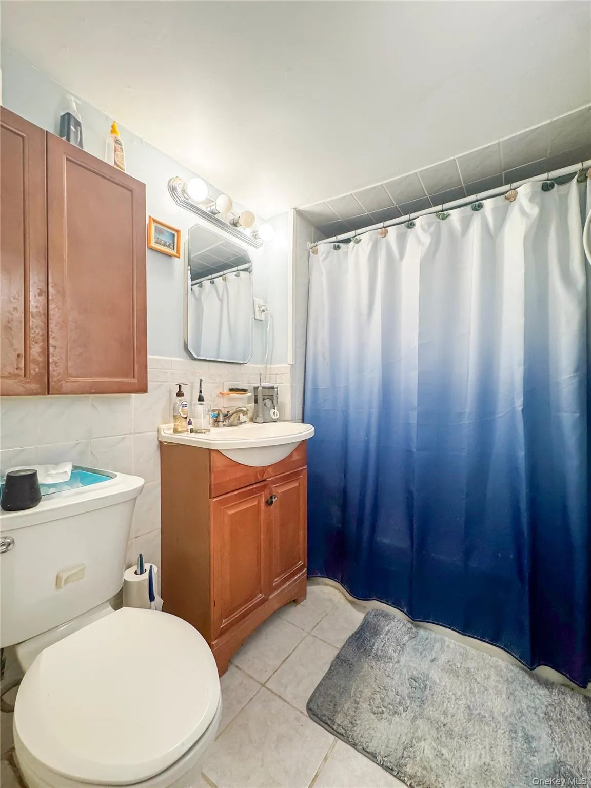 Full bath featuring vanity, light tile patterned flooring, tile walls, and curtained shower Full bath featuring vanity, light tile patterned flooring, tile walls, and curtained shower