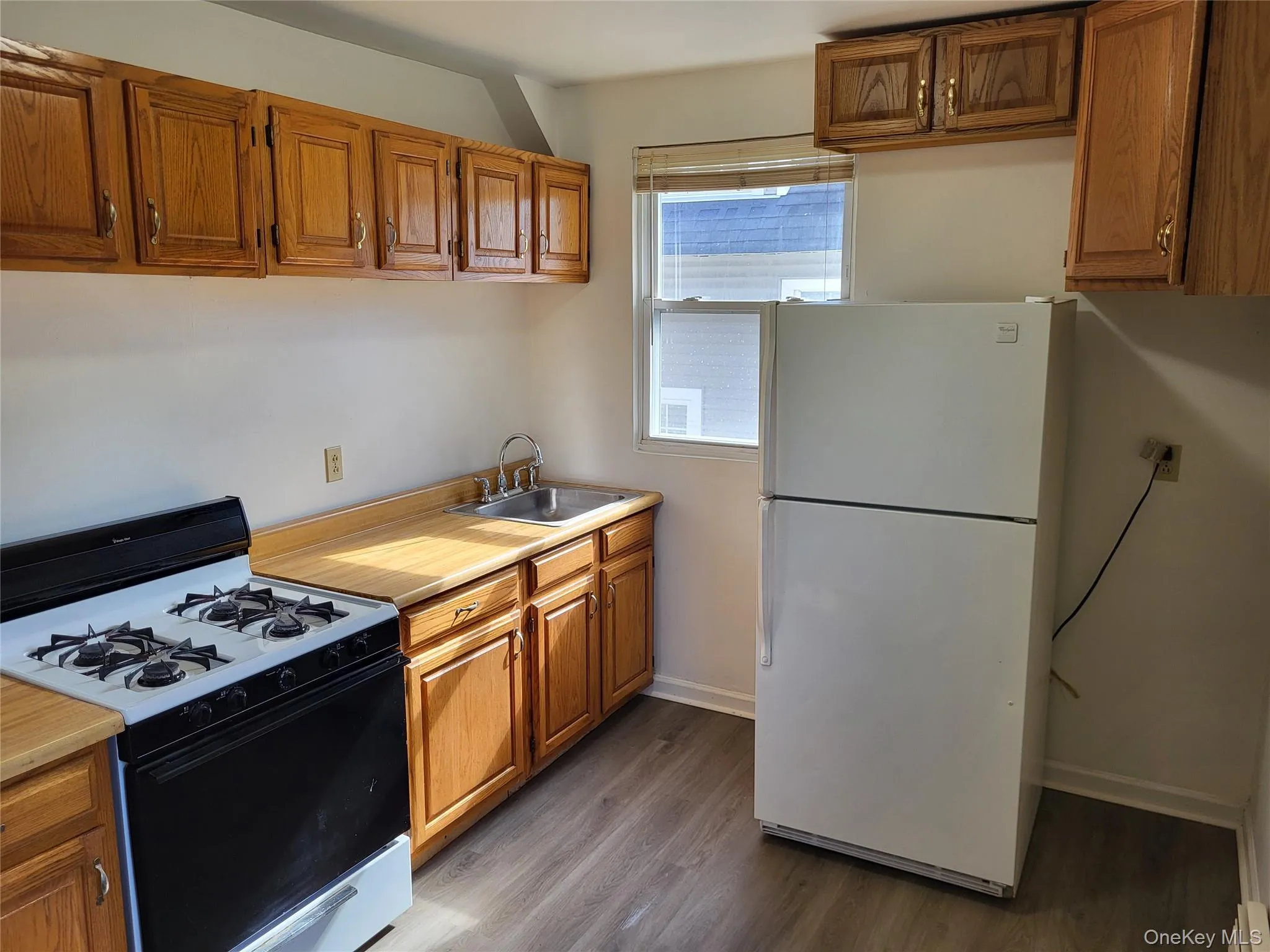 Kitchen featuring range with gas cooktop, freestanding refrigerator, brown cabinets, and light countertops Kitchen featuring range with gas cooktop, freestanding refrigerator, brown cabinets, and light countertops