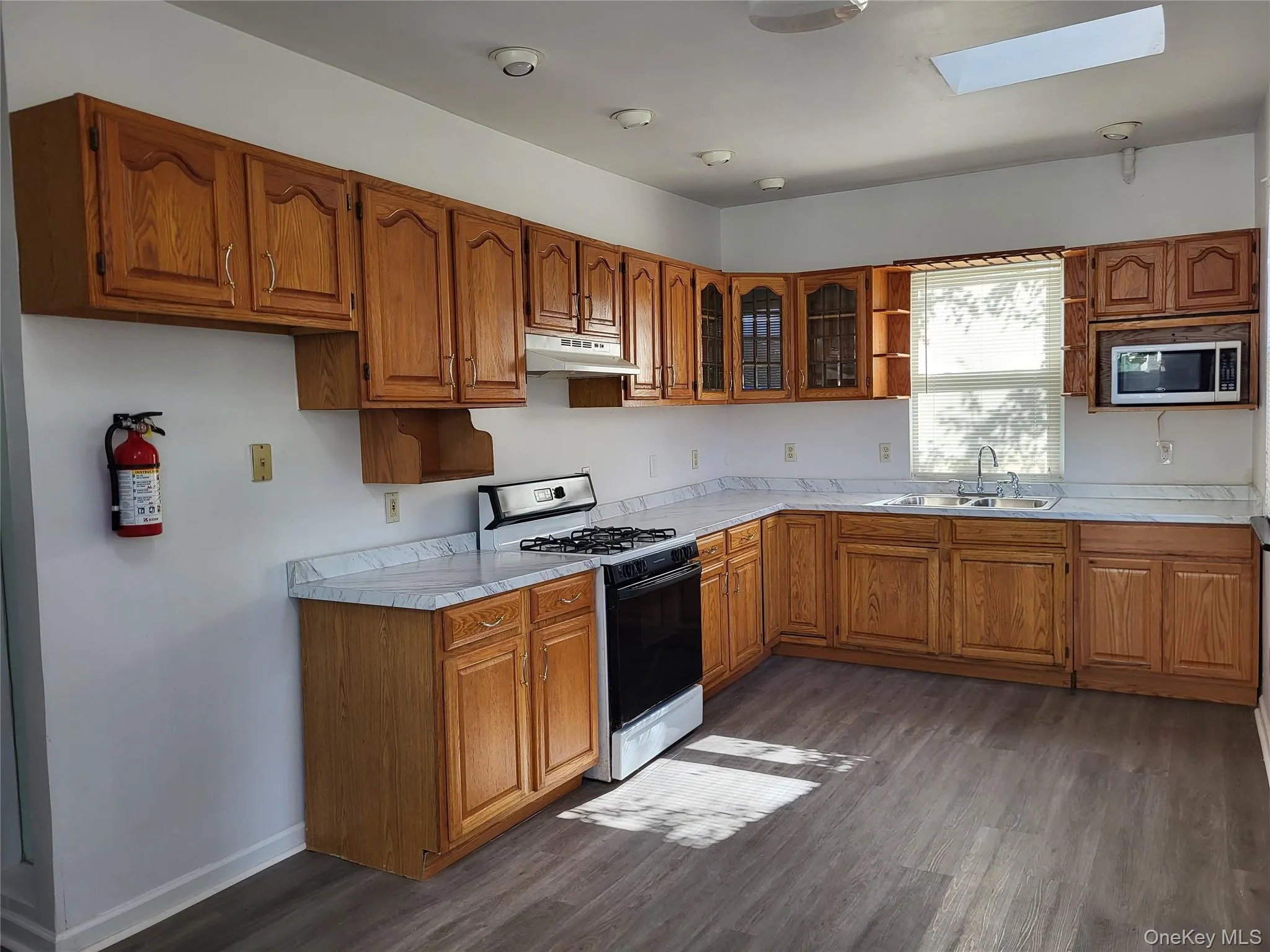 Kitchen with brown cabinetry, gas range oven, light countertops, dark wood finished floors, and open shelves Kitchen with brown cabinetry, gas range oven, light countertops, dark wood finished floors, and open shelves