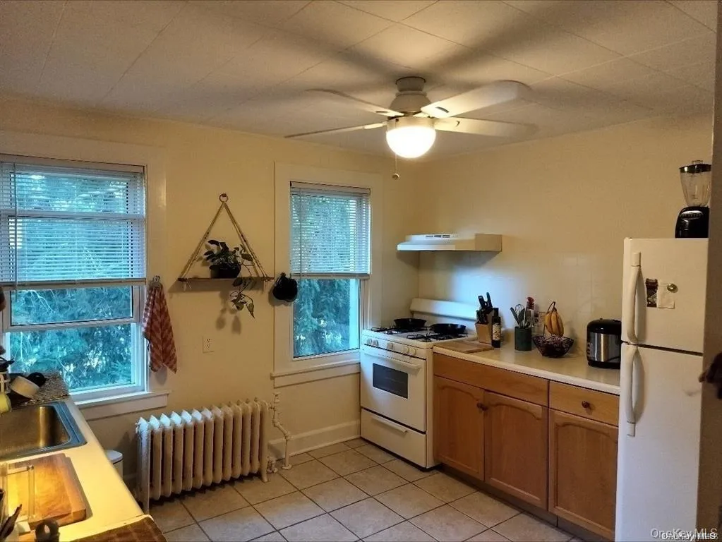 Kitchen featuring white appliances, light countertops, radiator heating unit, light tile patterned floors, and a ceiling fan Kitchen featuring white appliances, light countertops, radiator heating unit, light tile patterned floors, and a ceiling fan