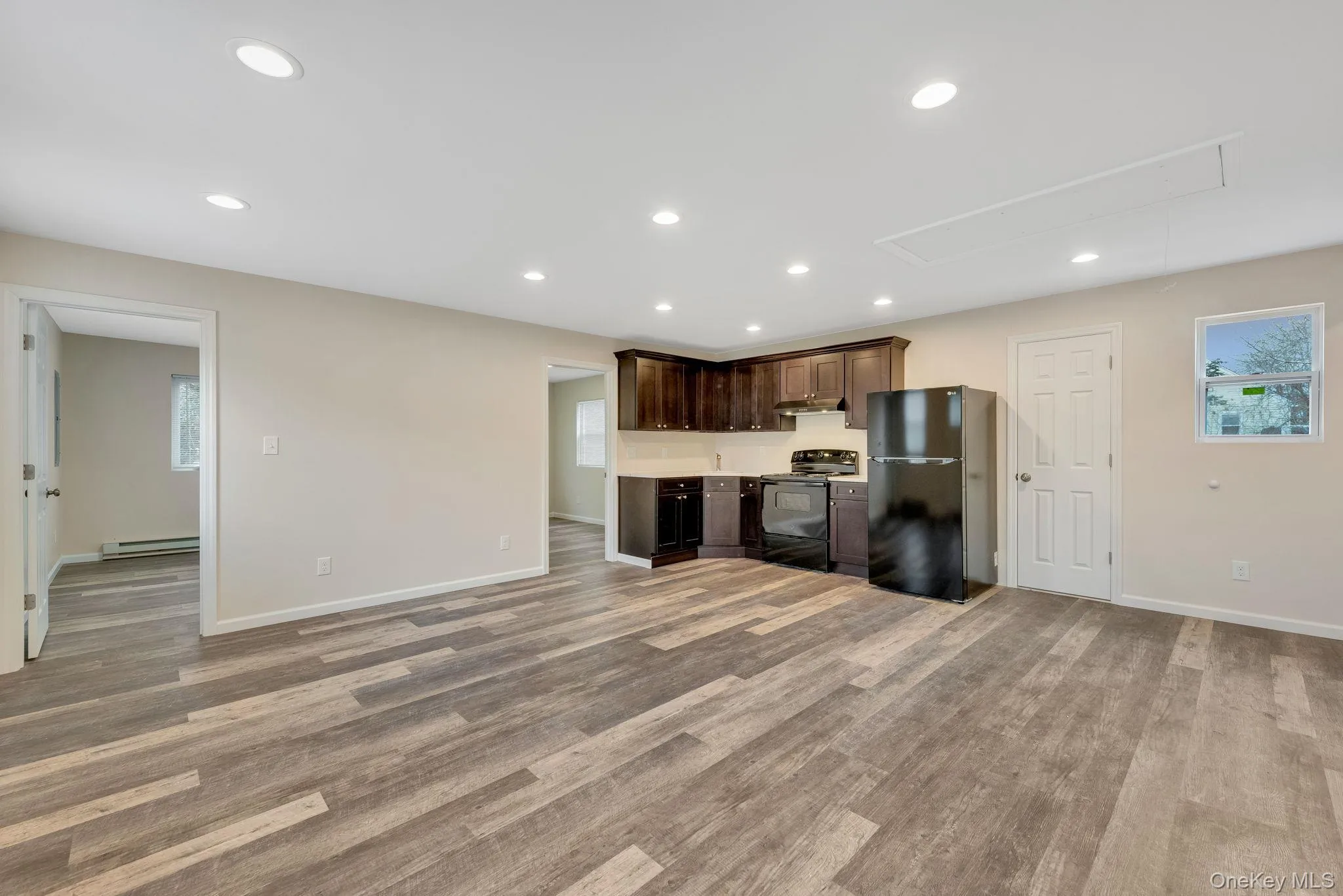 Unfurnished living room featuring healthy amount of natural light, recessed lighting, attic access, light wood-type flooring, and baseboard heating Unfurnished living room featuring healthy amount of natural light, recessed lighting, attic access, light wood-type flooring, and baseboard heating