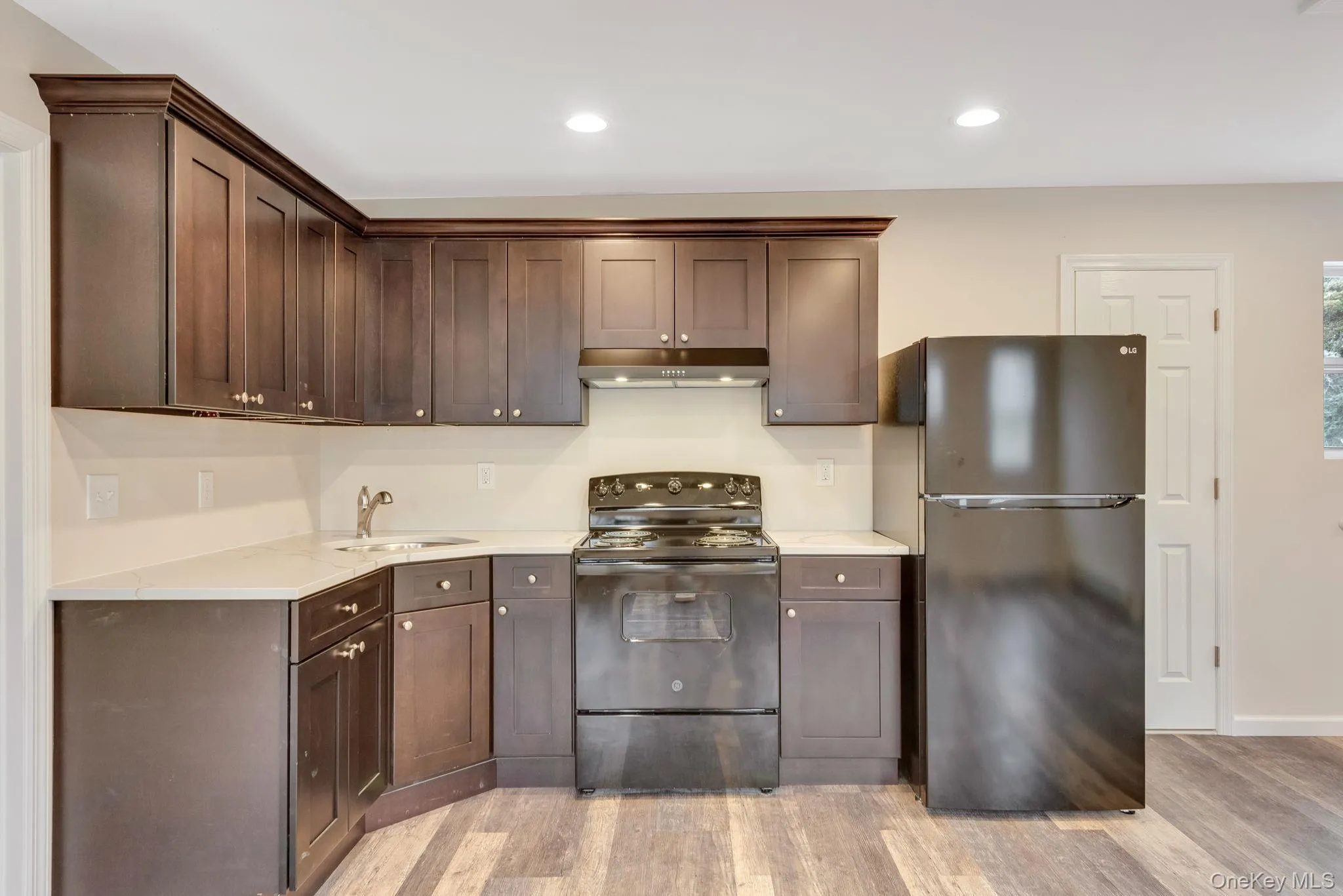 Kitchen featuring black appliances, light wood-type flooring, dark brown cabinets, under cabinet range hood, and recessed lighting Kitchen featuring black appliances, light wood-type flooring, dark brown cabinets, under cabinet range hood, and recessed lighting
