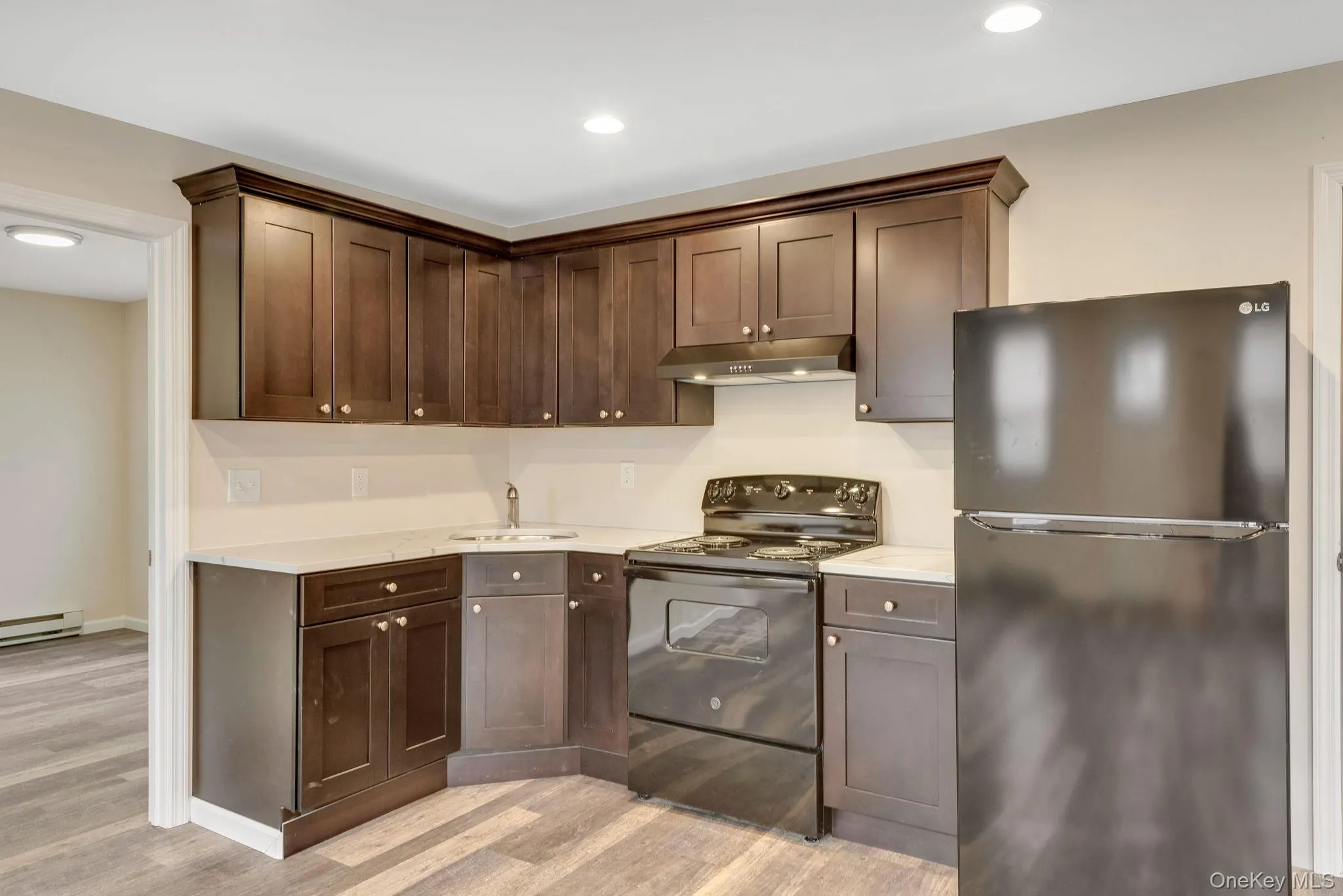 Kitchen featuring freestanding refrigerator, black electric range, light wood-style flooring, dark brown cabinets, and under cabinet range hood Kitchen featuring freestanding refrigerator, black electric range, light wood-style flooring, dark brown cabinets, and under cabinet range hood