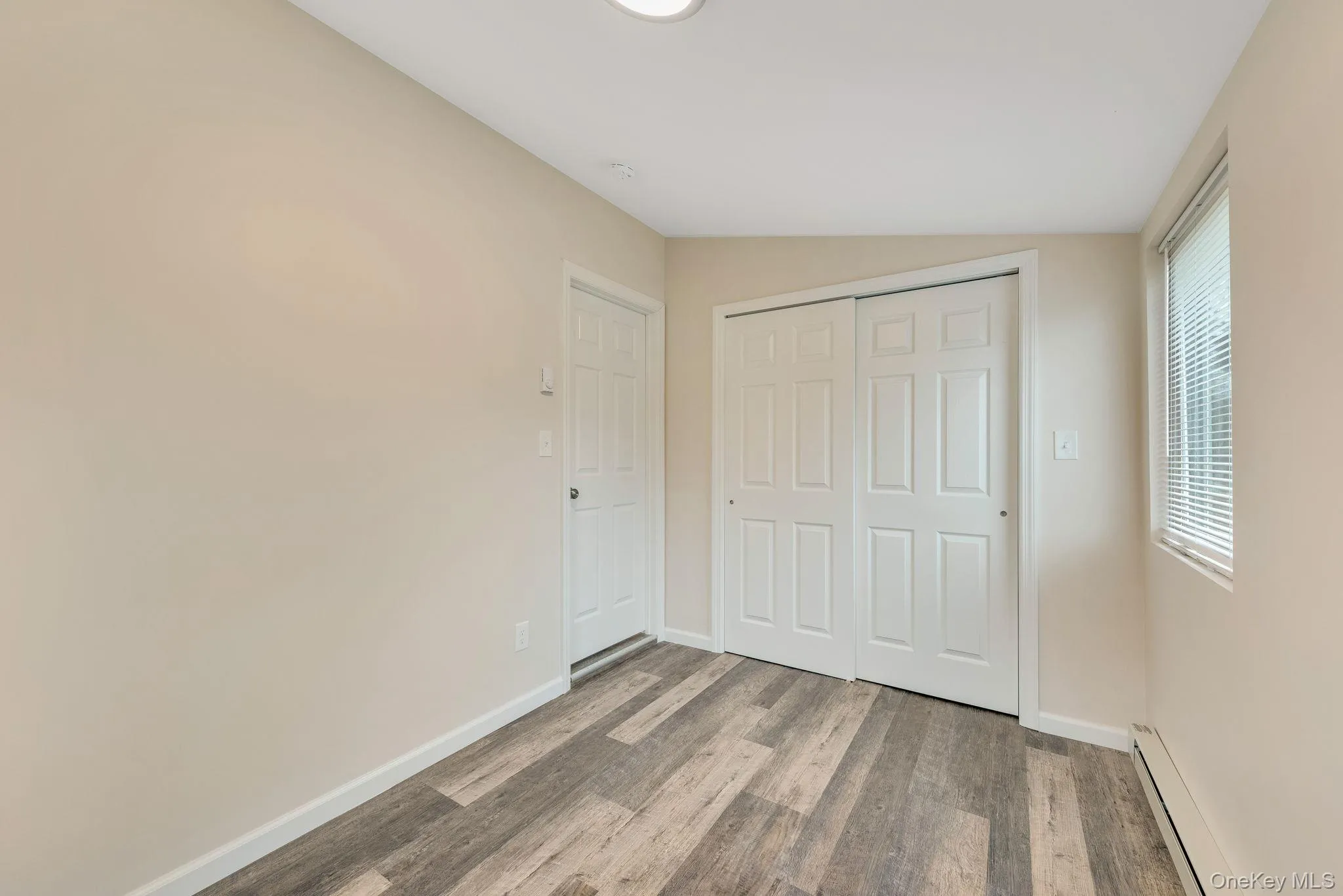 Unfurnished bedroom with baseboard heating, light wood-type flooring, and a closet Unfurnished bedroom with baseboard heating, light wood-type flooring, and a closet