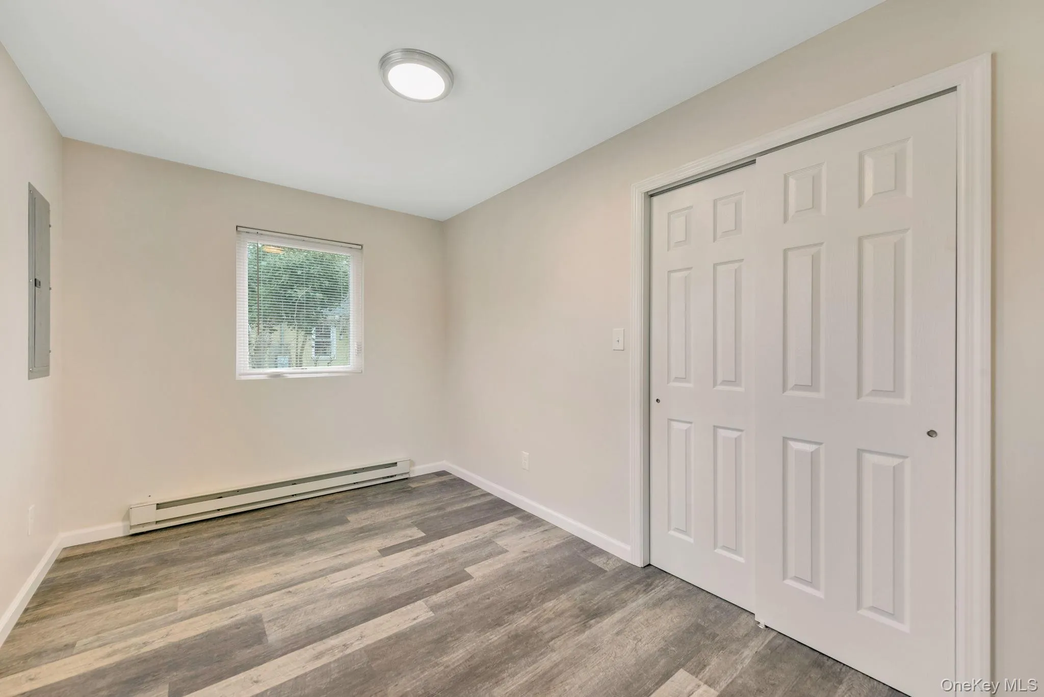 Unfurnished bedroom with a baseboard heating unit, light wood-style flooring, a closet, and electric panel Unfurnished bedroom with a baseboard heating unit, light wood-style flooring, a closet, and electric panel