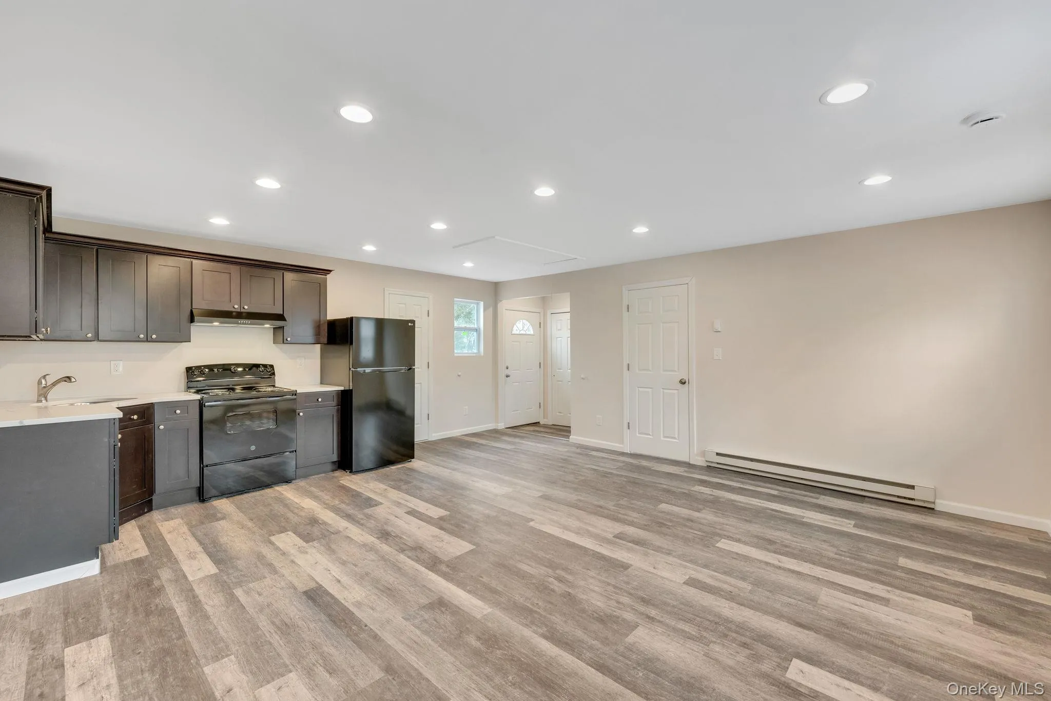 Kitchen featuring black appliances, recessed lighting, a baseboard heating unit, light wood-type flooring, and dark brown cabinetry Kitchen featuring black appliances, recessed lighting, a baseboard heating unit, light wood-type flooring, and dark brown cabinetry