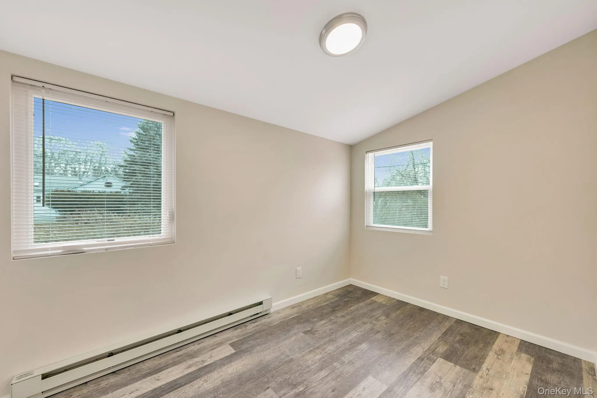 Unfurnished room featuring a baseboard radiator, lofted ceiling, and wood finished floors Unfurnished room featuring a baseboard radiator, lofted ceiling, and wood finished floors