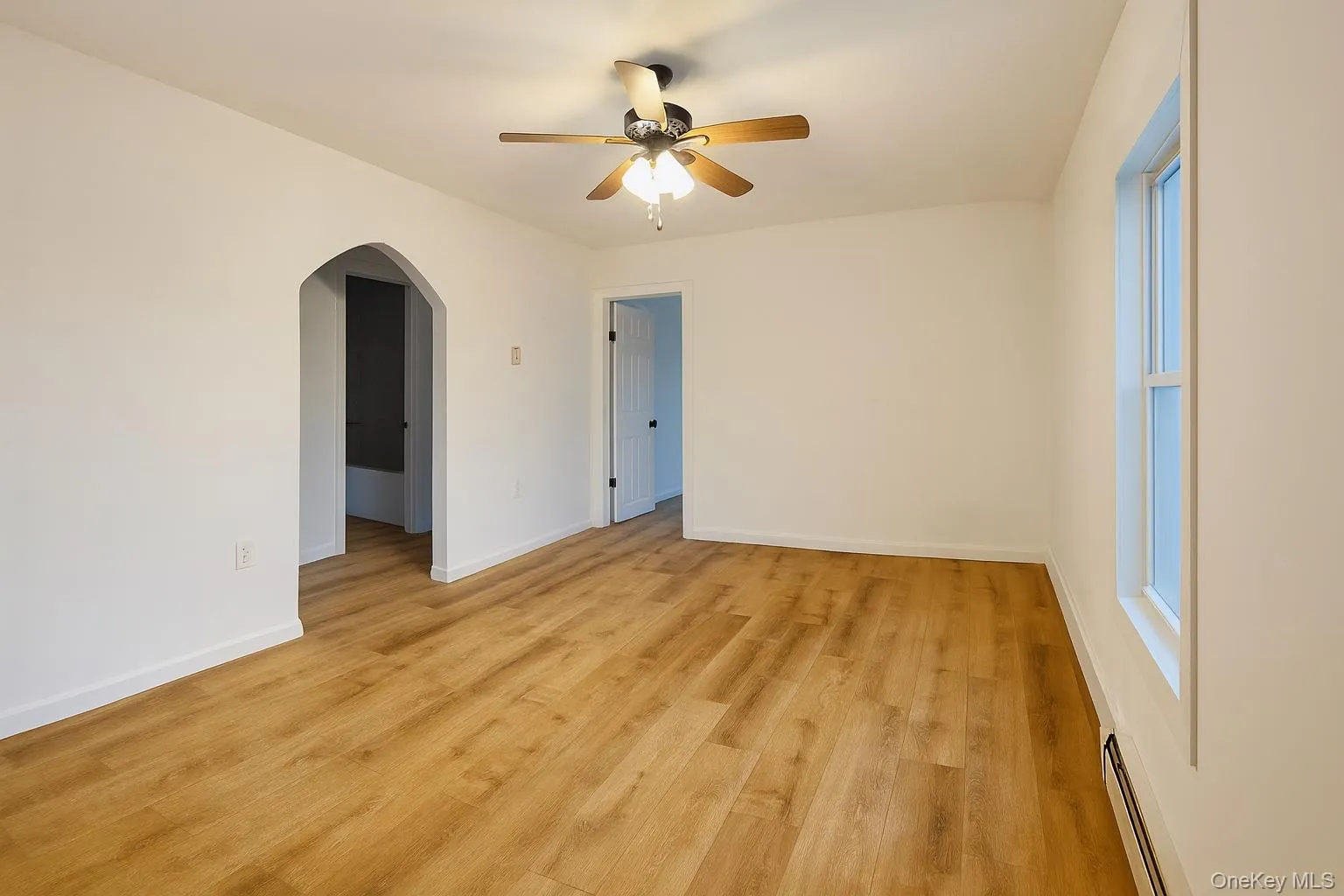 Spare room featuring baseboard heating, light wood-style floors, arched walkways, and ceiling fan Spare room featuring baseboard heating, light wood-style floors, arched walkways, and ceiling fan