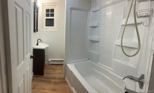 Full bath featuring vanity, shower / washtub combination, wood finished floors, and baseboard heating Full bath featuring vanity, shower / washtub combination, wood finished floors, and baseboard heating