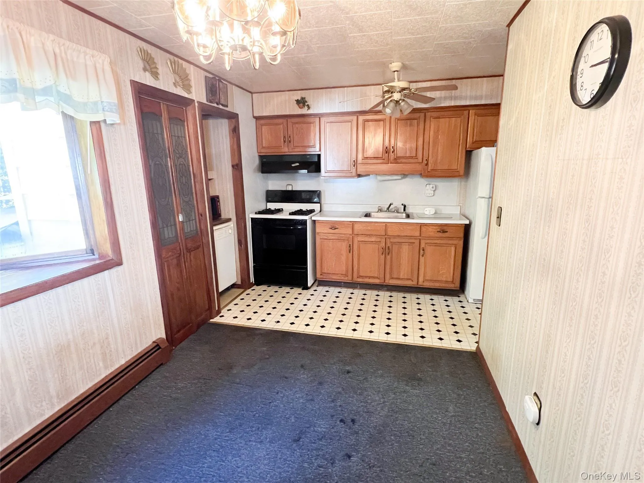 Kitchen with wallpapered walls, a baseboard heating unit, light countertops, range with gas stovetop, and dark colored carpet Kitchen with wallpapered walls, a baseboard heating unit, light countertops, range with gas stovetop, and dark colored carpet