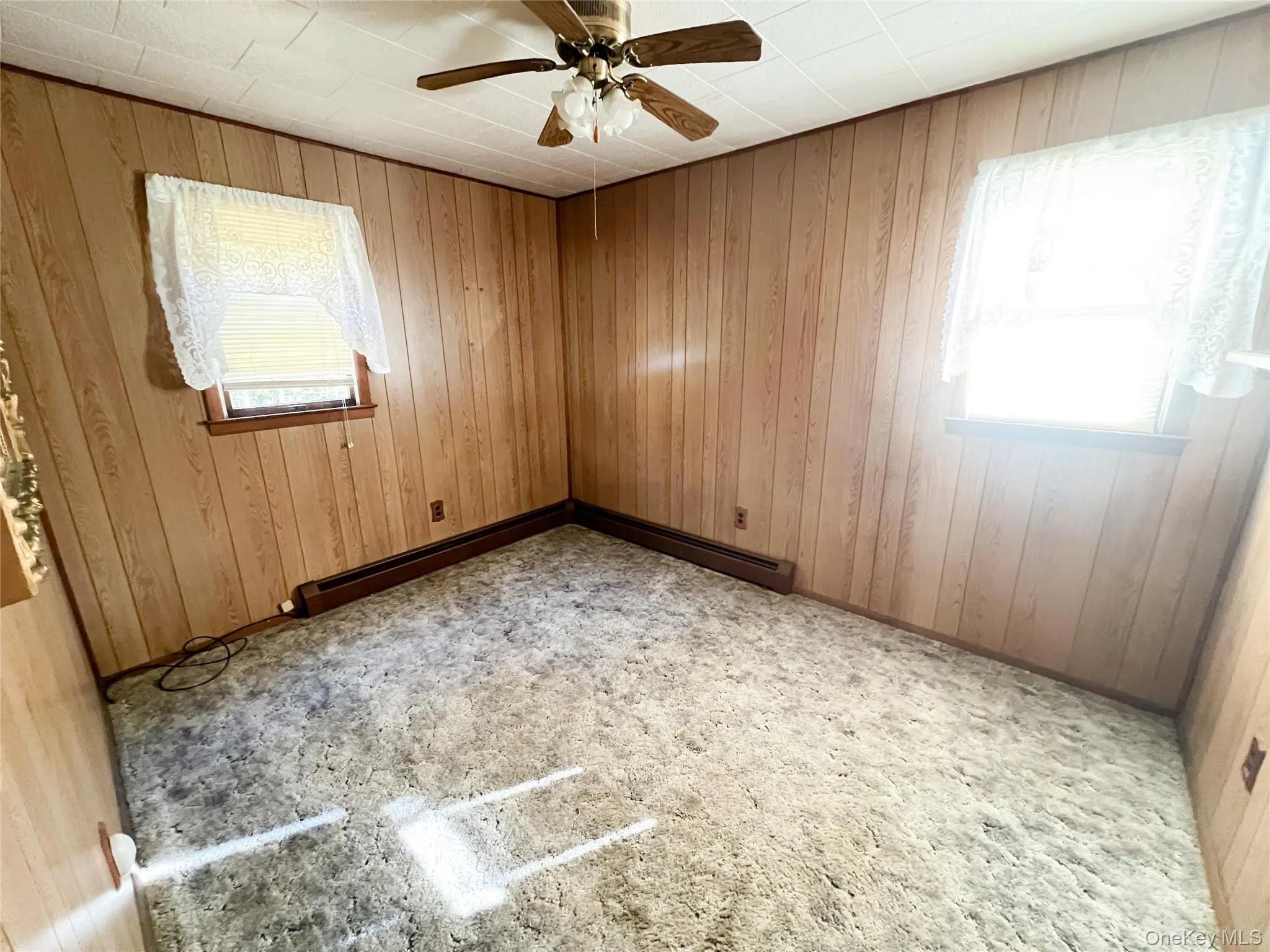 Empty room with wooden walls, ceiling fan, and a baseboard heating unit Empty room with wooden walls, ceiling fan, and a baseboard heating unit