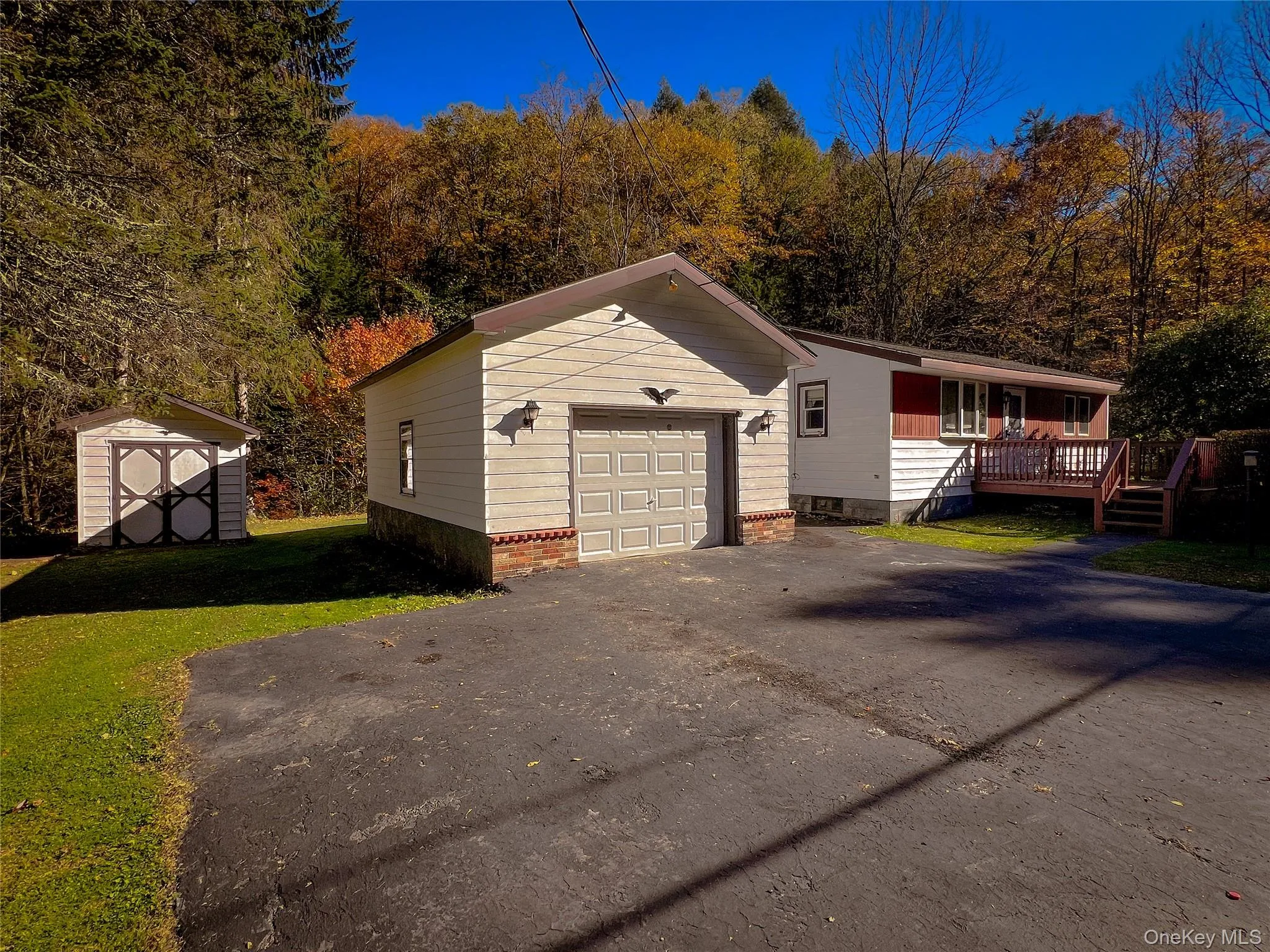 View of front of home with a wooden deck, a storage shed, asphalt driveway, and a front yard View of front of home with a wooden deck, a storage shed, asphalt driveway, and a front yard