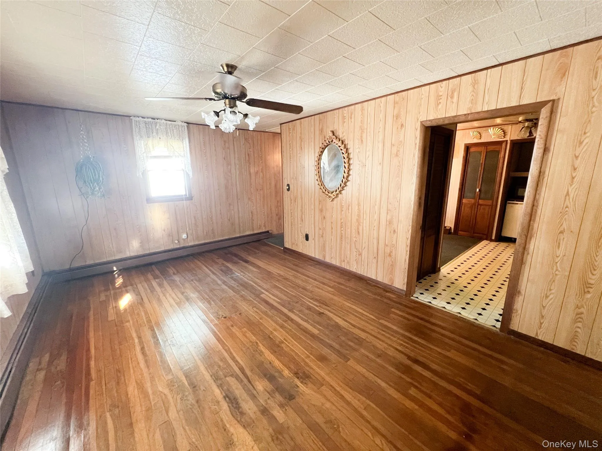 Spare room with wooden walls, dark wood-type flooring, a baseboard heating unit, and a ceiling fan Spare room with wooden walls, dark wood-type flooring, a baseboard heating unit, and a ceiling fan