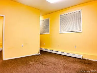 Empty room featuring dark colored carpet and a baseboard heating unit Empty room featuring dark colored carpet and a baseboard heating unit