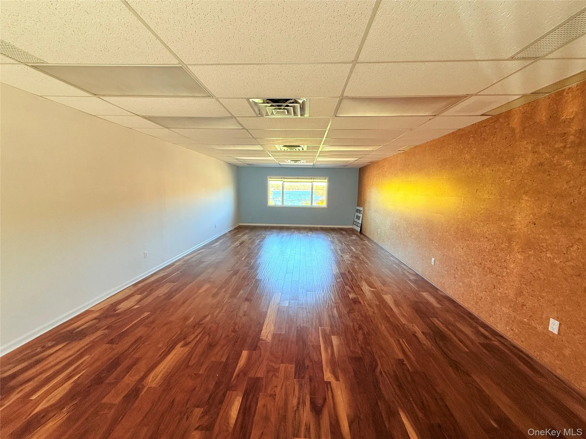 Unfurnished room featuring a paneled ceiling, baseboards, visible vents, and wood finished floors Unfurnished room featuring a paneled ceiling, baseboards, visible vents, and wood finished floors