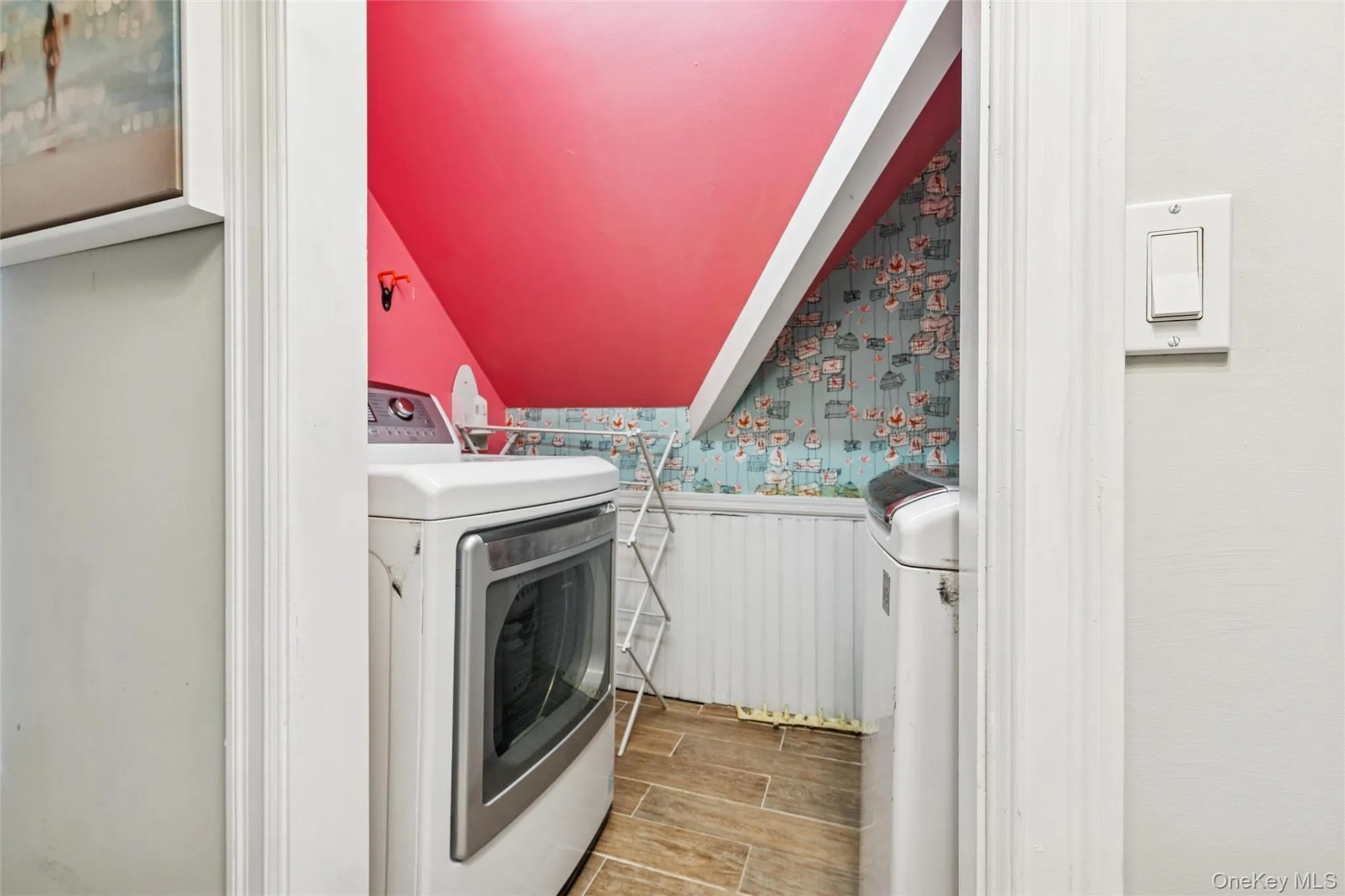 Laundry area with wood tiled floors, wallpapered walls, wainscoting, and washer and clothes dryer Laundry area with wood tiled floors, wallpapered walls, wainscoting, and washer and clothes dryer