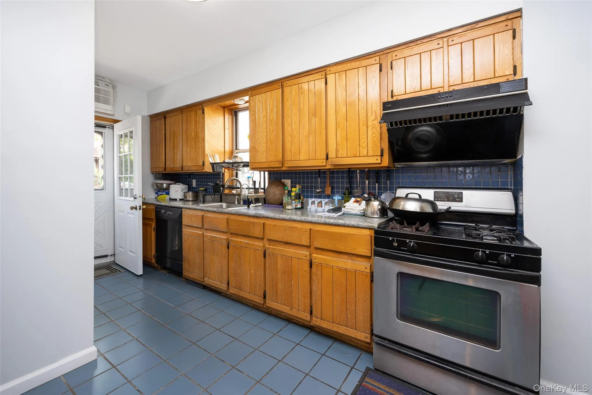 Kitchen with stainless steel gas range oven, backsplash, exhaust hood, light countertops, and dark tile patterned floors Kitchen with stainless steel gas range oven, backsplash, exhaust hood, light countertops, and dark tile patterned floors
