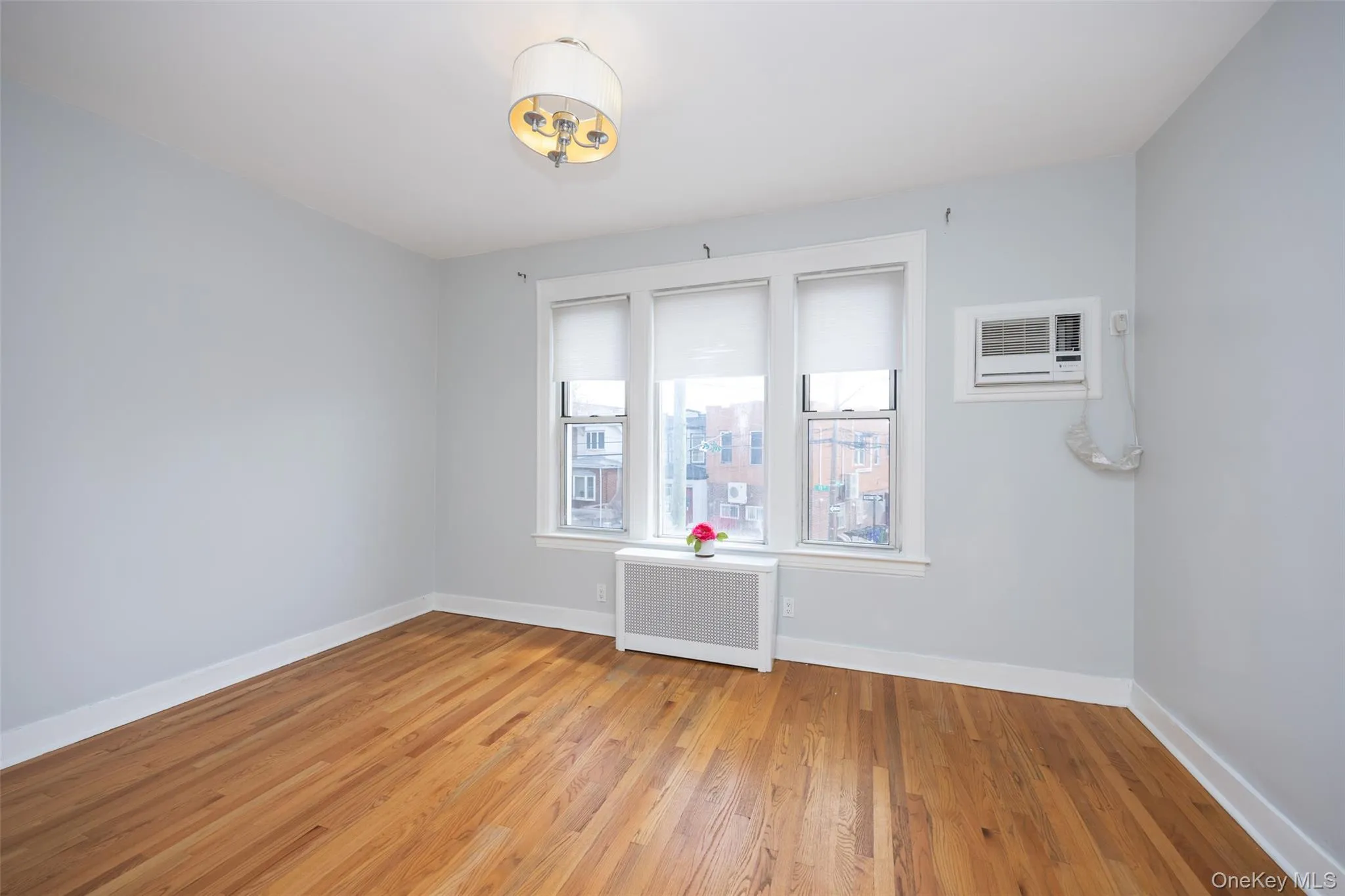 Empty room with radiator heating unit, wood finished floors, and a wall mounted AC Empty room with radiator heating unit, wood finished floors, and a wall mounted AC