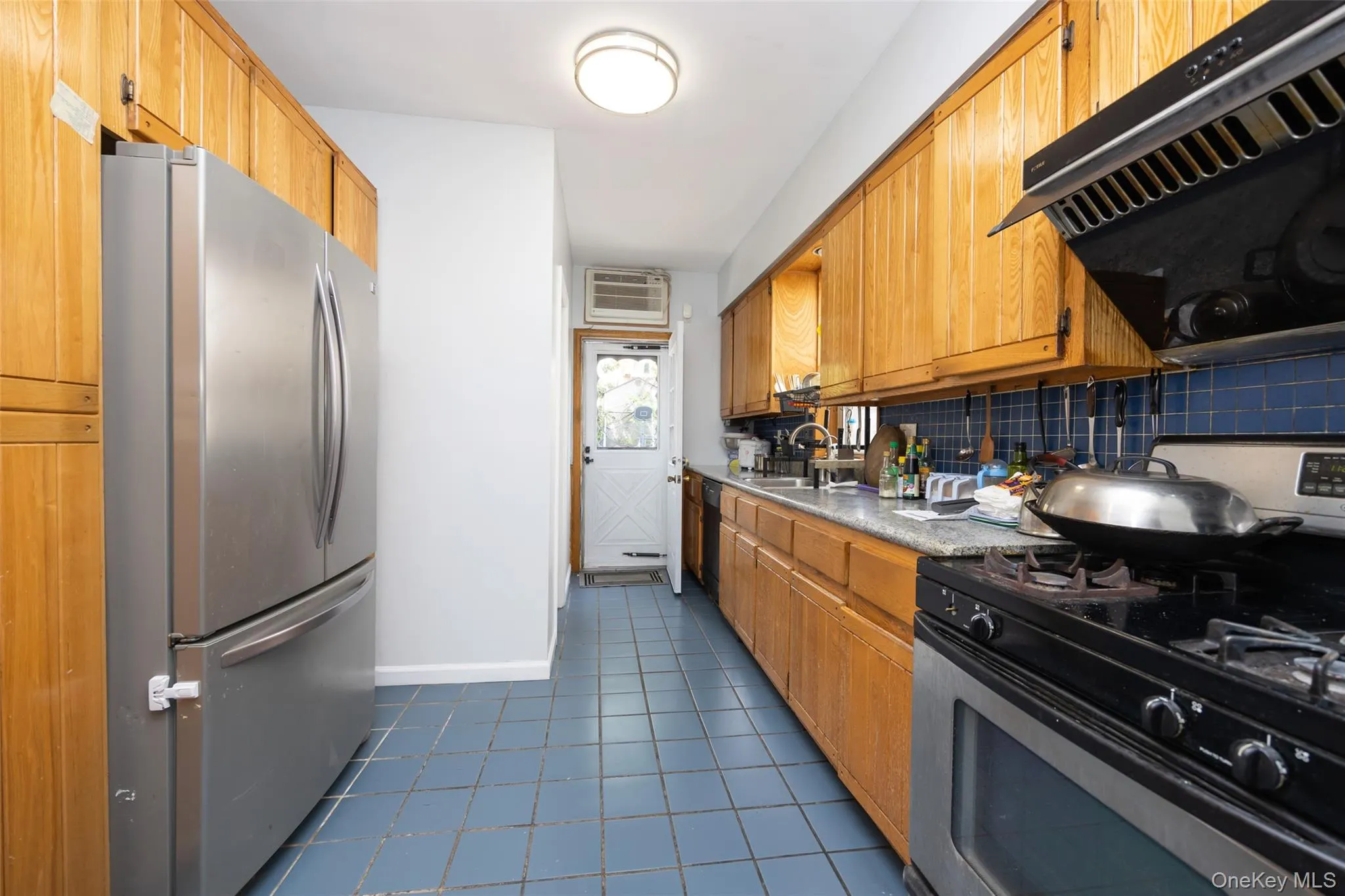 Kitchen with stainless steel appliances, exhaust hood, brown cabinetry, dark tile patterned flooring, and light countertops Kitchen with stainless steel appliances, exhaust hood, brown cabinetry, dark tile patterned flooring, and light countertops