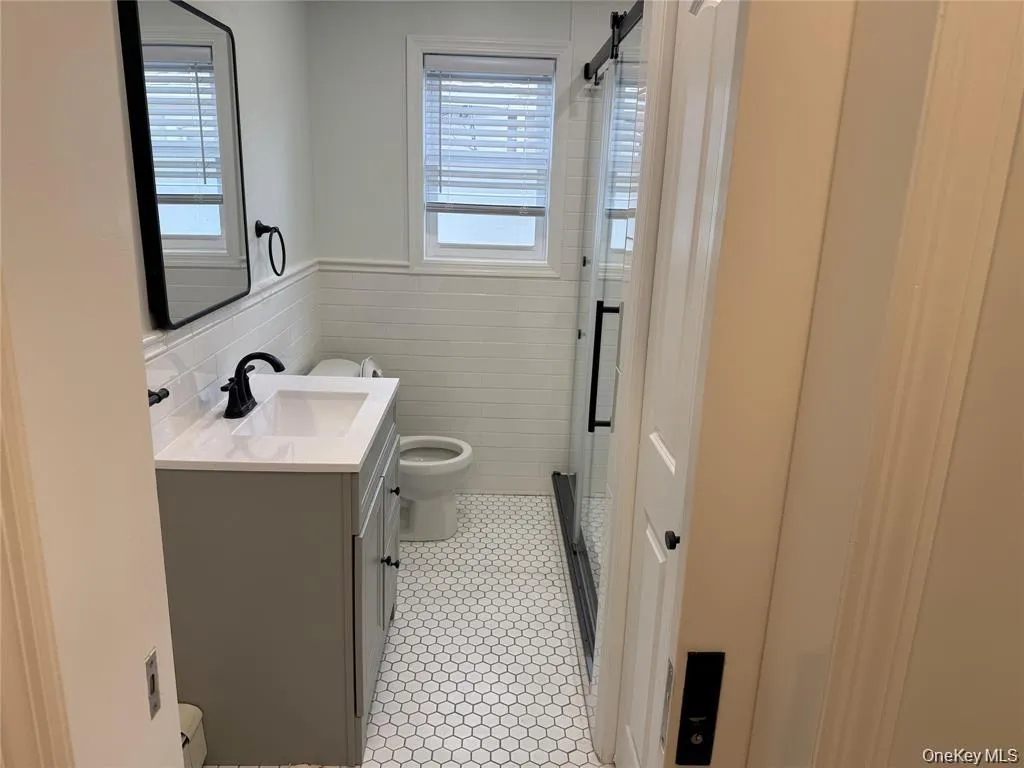 Bathroom with vanity, a shower stall, tile walls, light tile patterned flooring, and wainscoting Bathroom with vanity, a shower stall, tile walls, light tile patterned flooring, and wainscoting